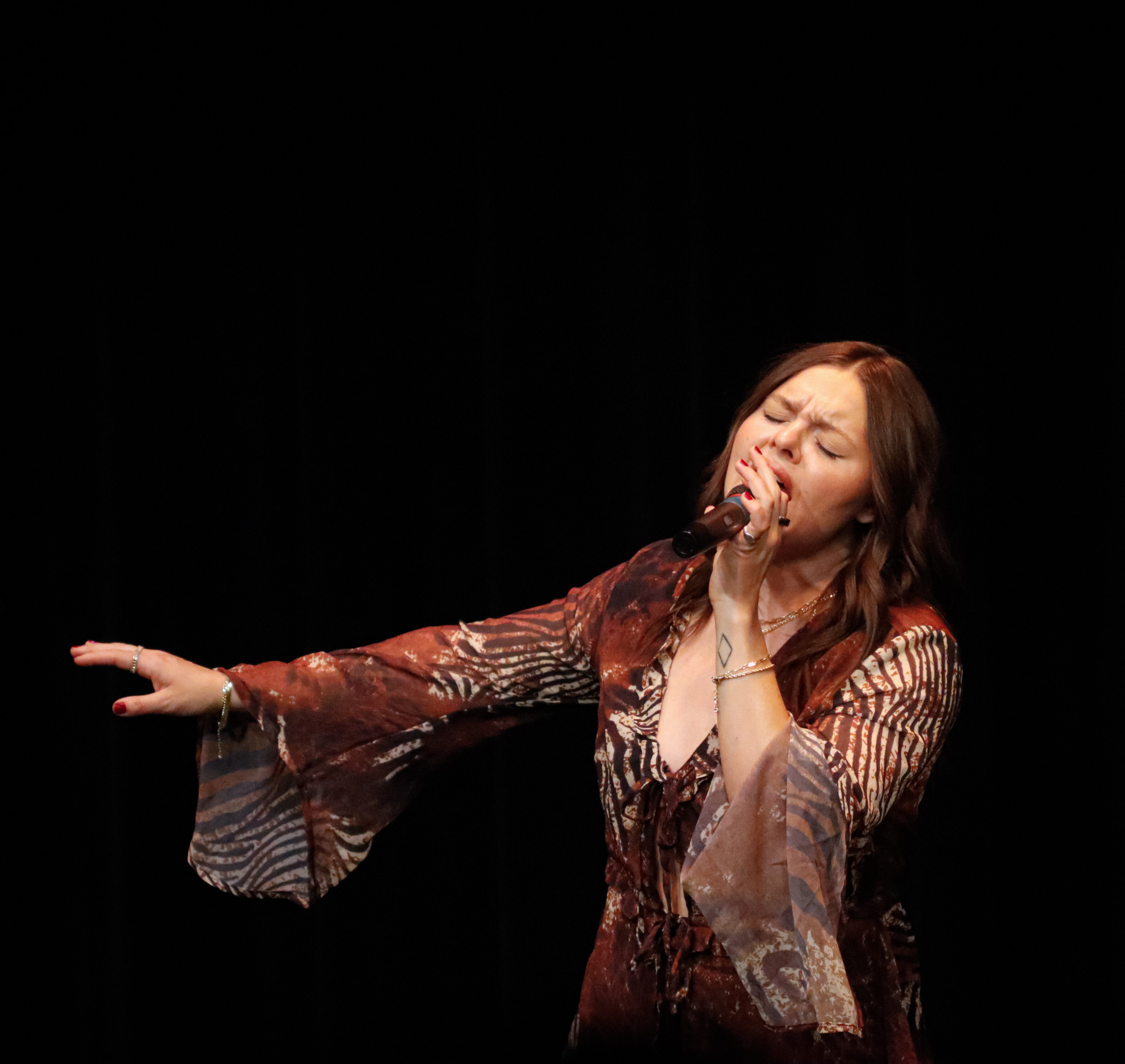 Parker Graye performing on stage, passionately singing into a microphone while dressed in a flowing, patterned outfit.