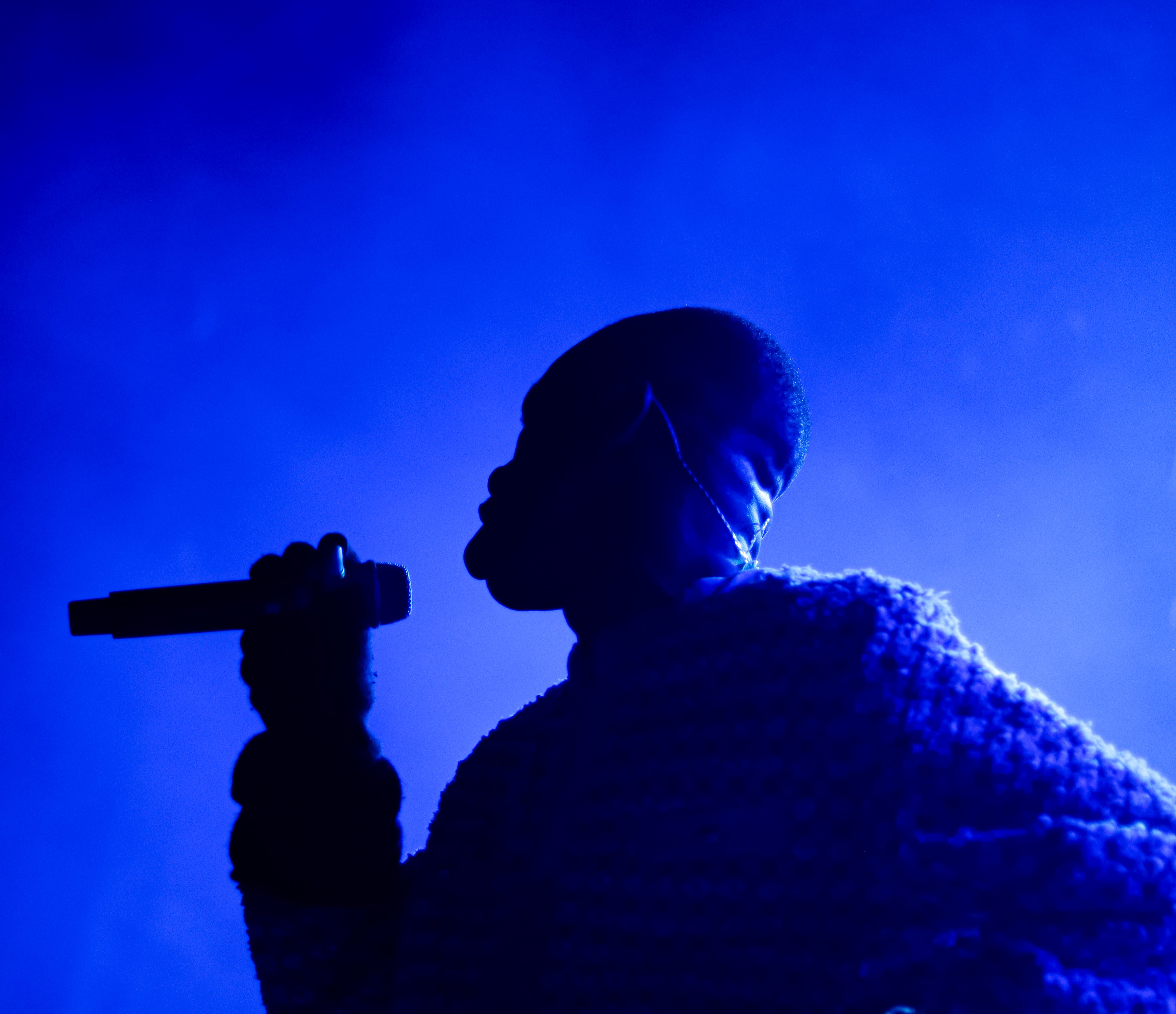 A performer singing into a microphone on stage, silhouetted against a blue and foggy backdrop.