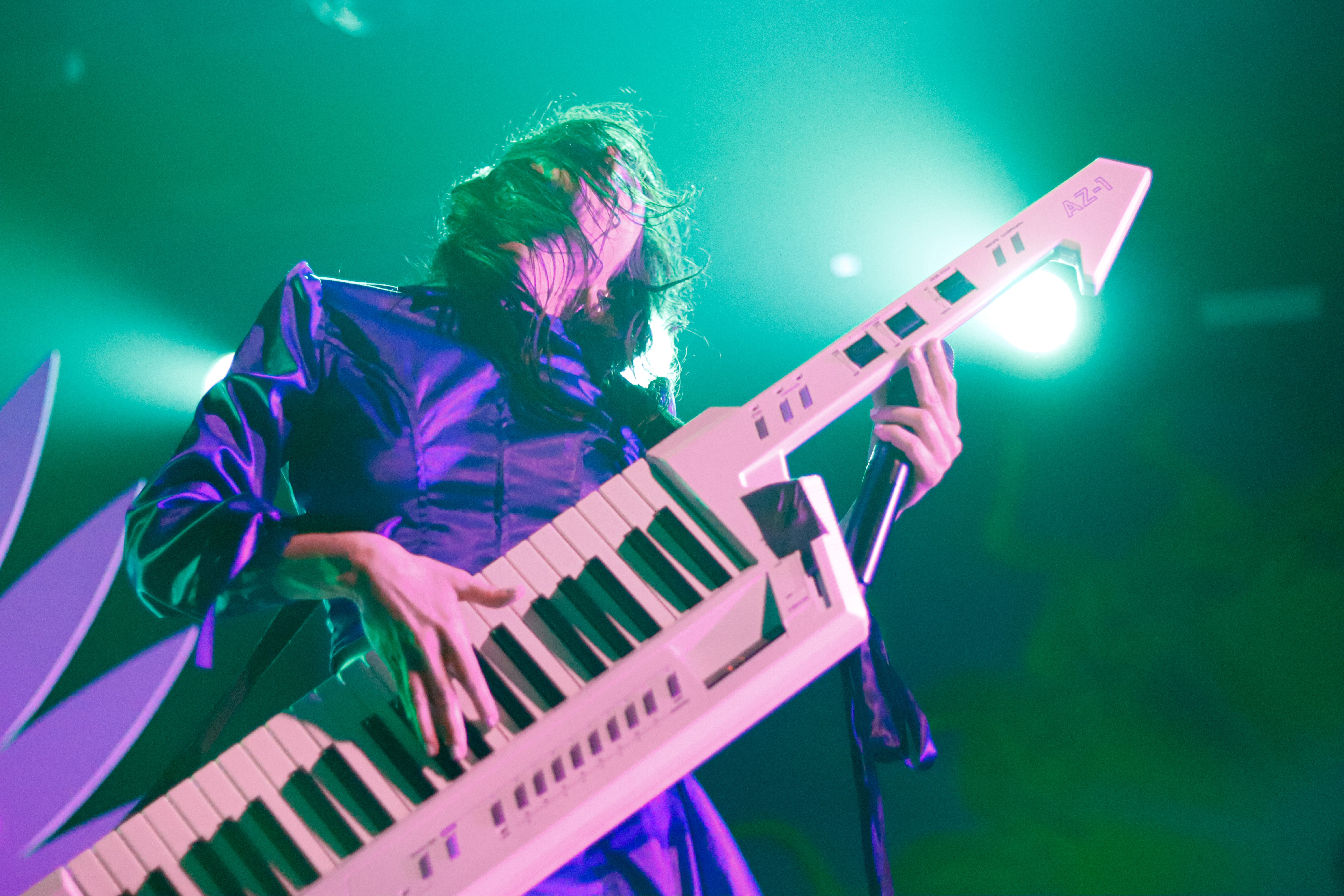 A musician performing on stage with a keytar, wearing a shiny blue outfit, under vibrant lighting that creates an energetic atmosphere.