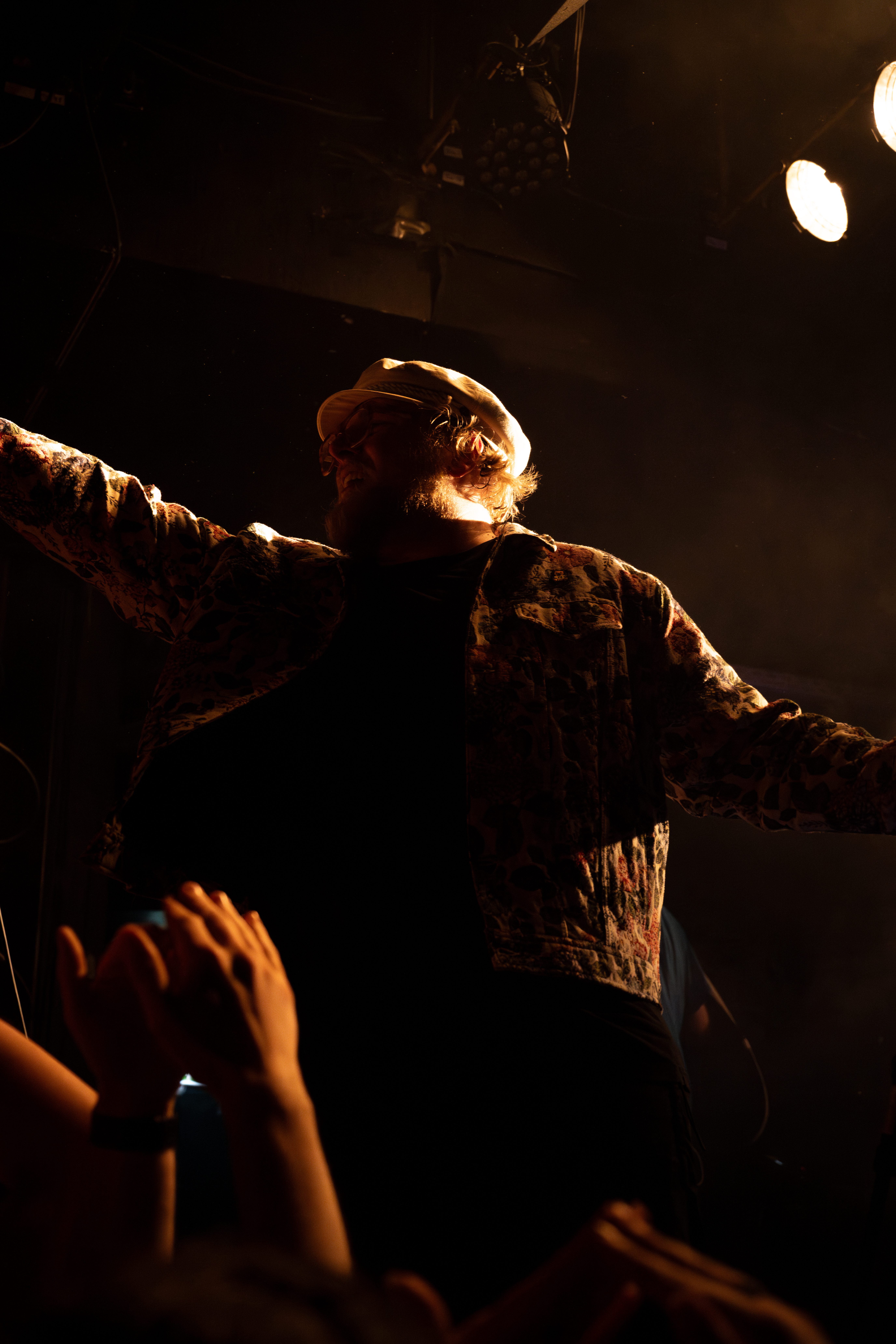 A performer on stage with arms outstretched, surrounded by hands reaching out from the audience under dramatic lighting.