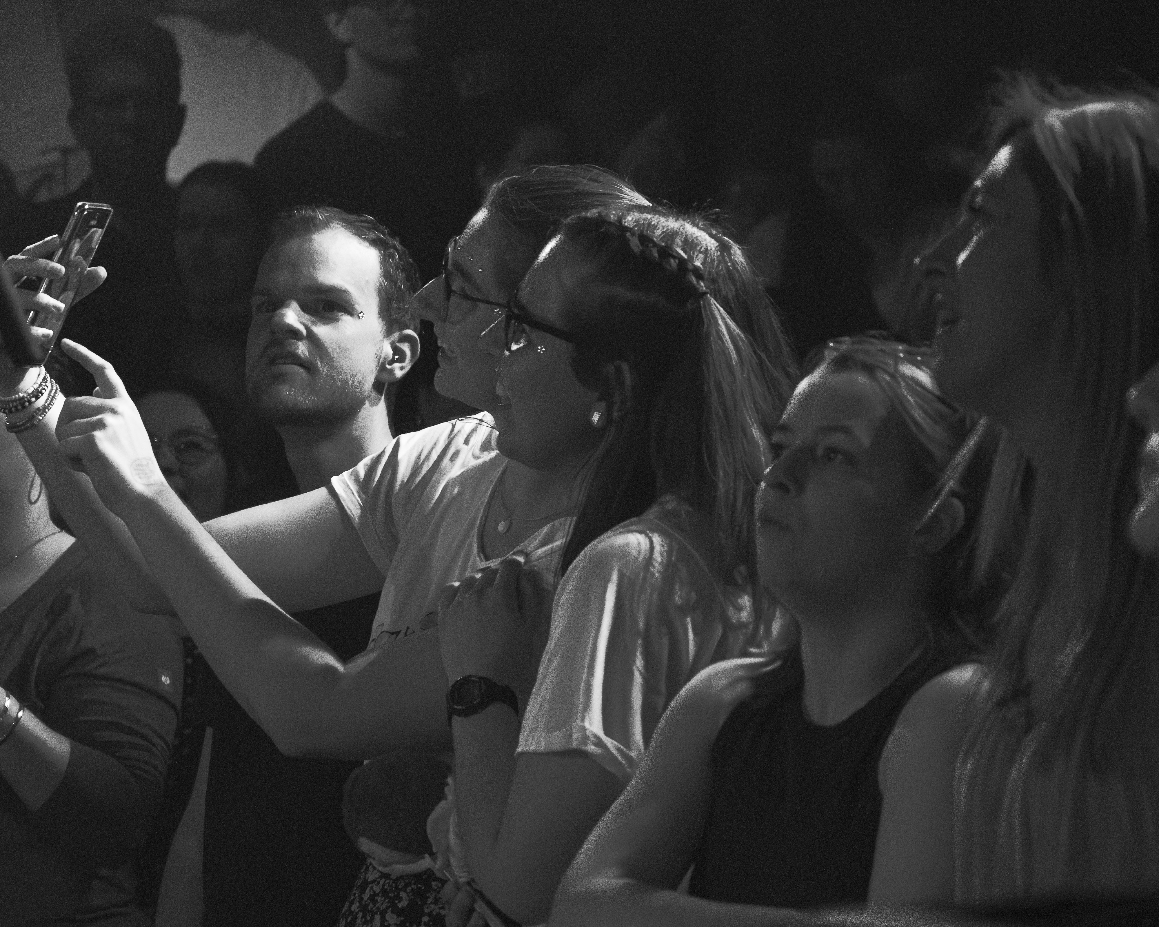 A group of people at a concert, focused on taking photos and enjoying the performance, captured in black and white.