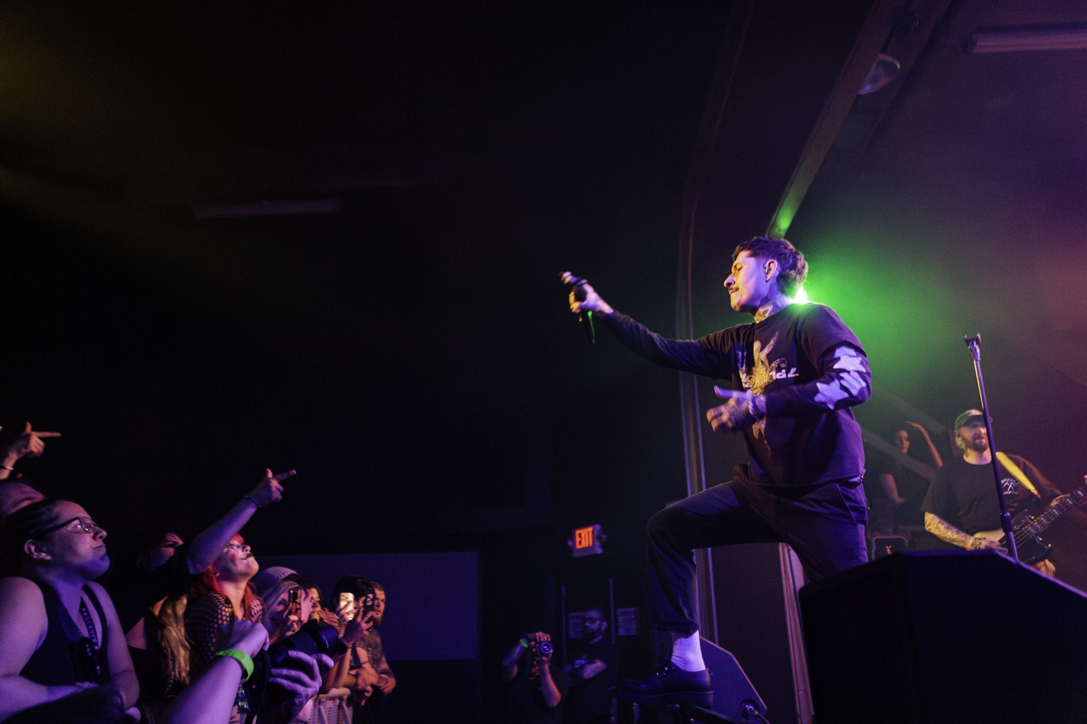 A performer singing on stage with a microphone, while the audience reacts enthusiastically, some with hands raised.