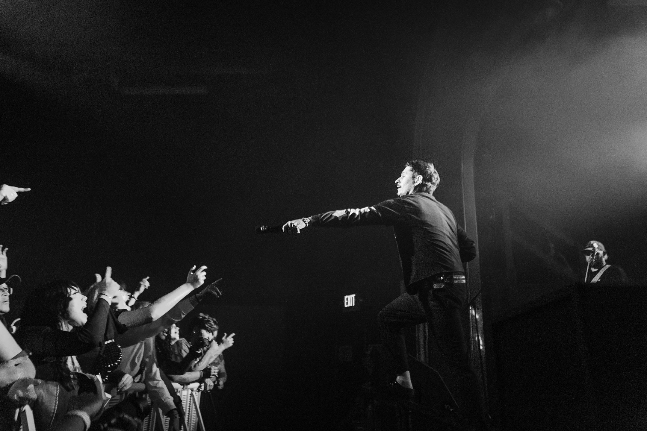 A musician performing on stage with a microphone, engaging with an enthusiastic crowd in a dimly lit venue.