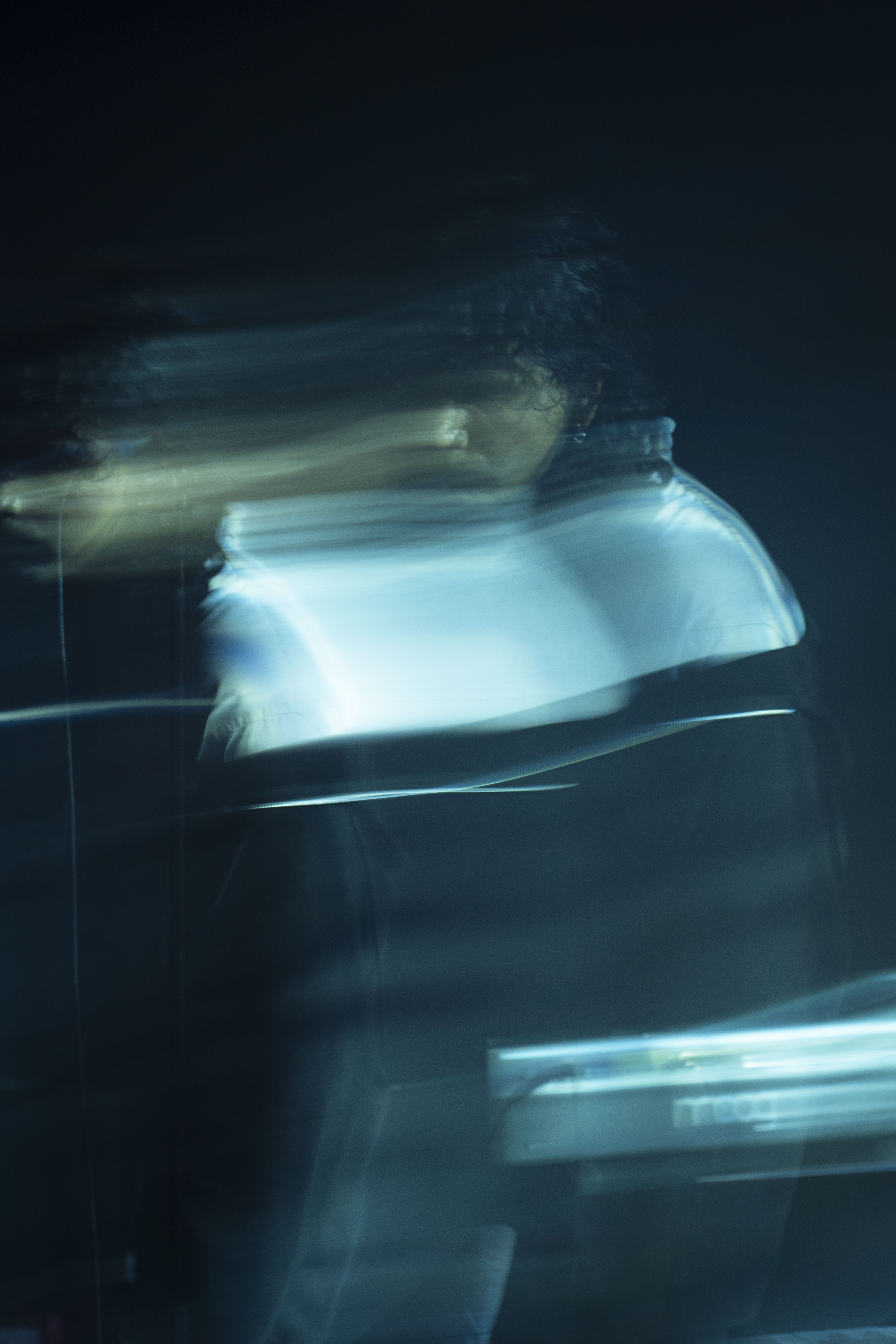 A blurred image of a musician on stage, with movement captured creating an ethereal effect, suggesting energy and emotion during a performance.