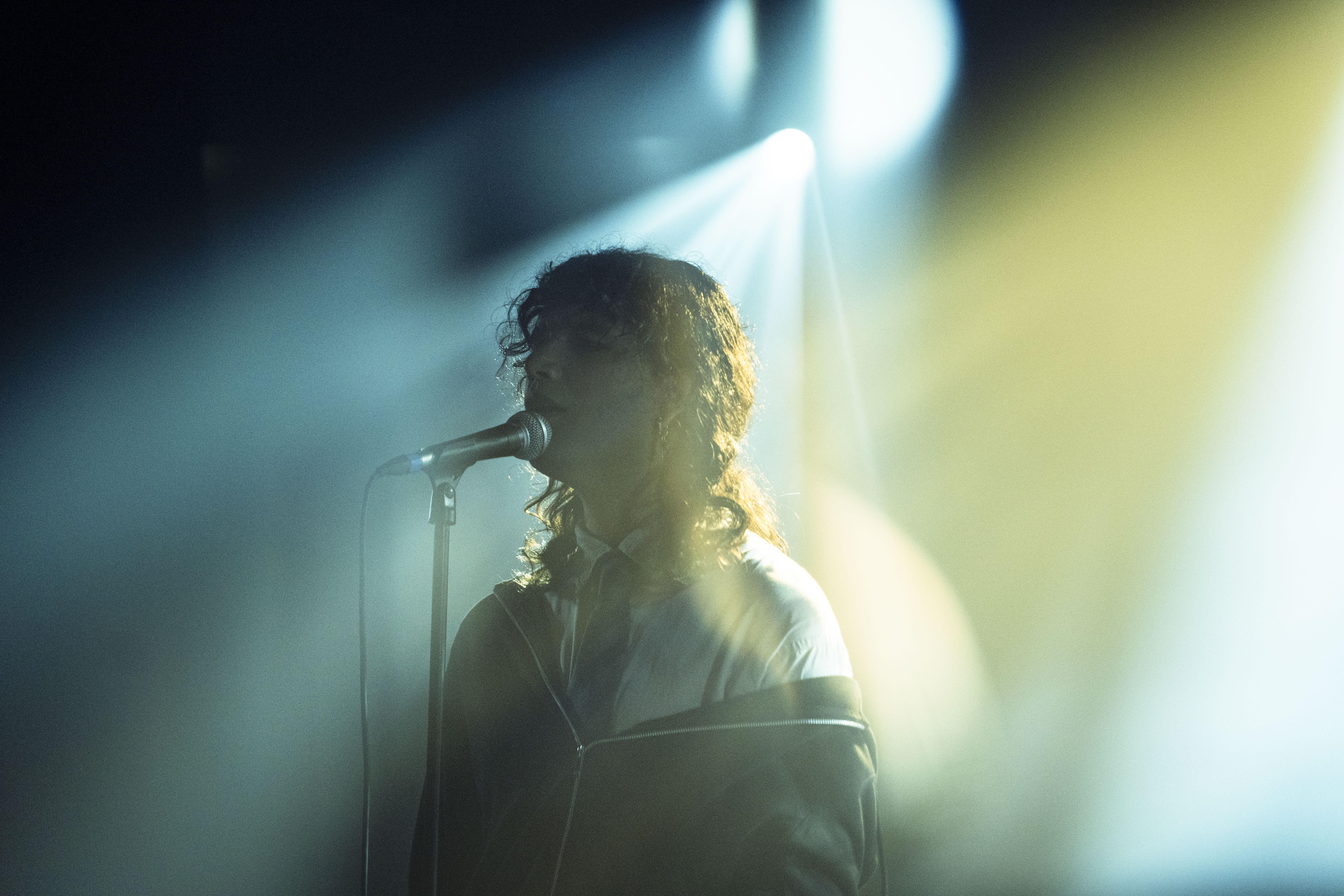 A performer sings into a microphone on stage, illuminated by soft, colorful lighting.