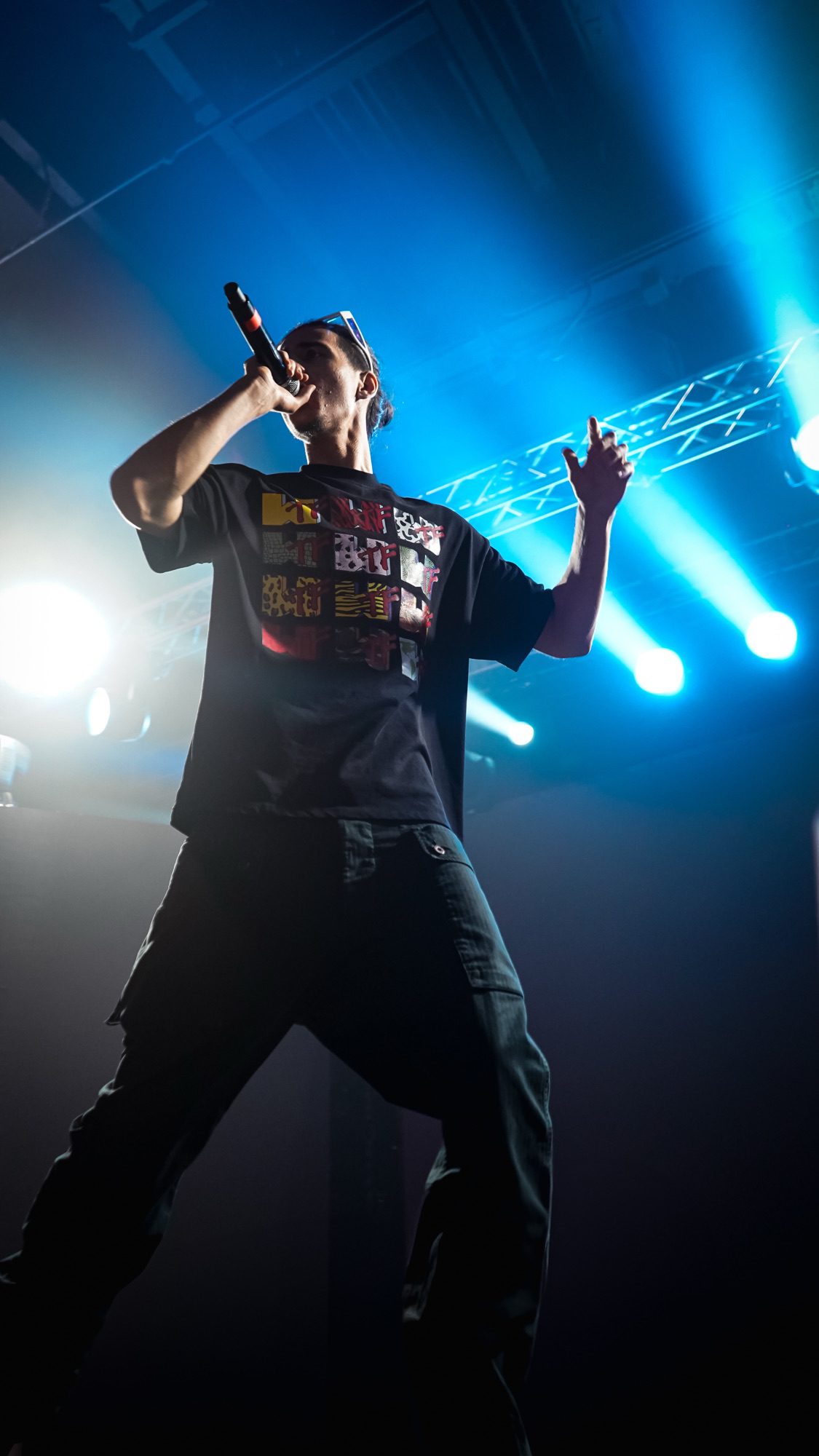 A performer singing into a microphone on stage, illuminated by vibrant blue lights, exuding energy and passion.
