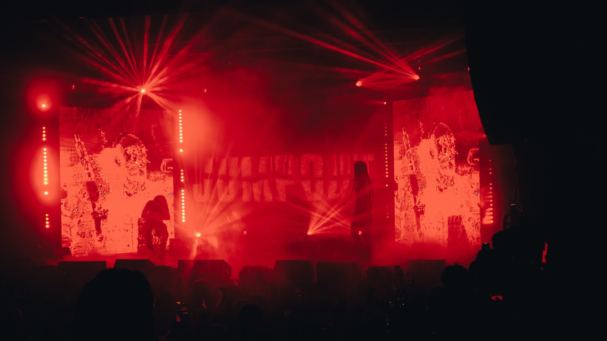 A performer on stage with dramatic red lighting and visual effects, engaging the crowd at a concert.