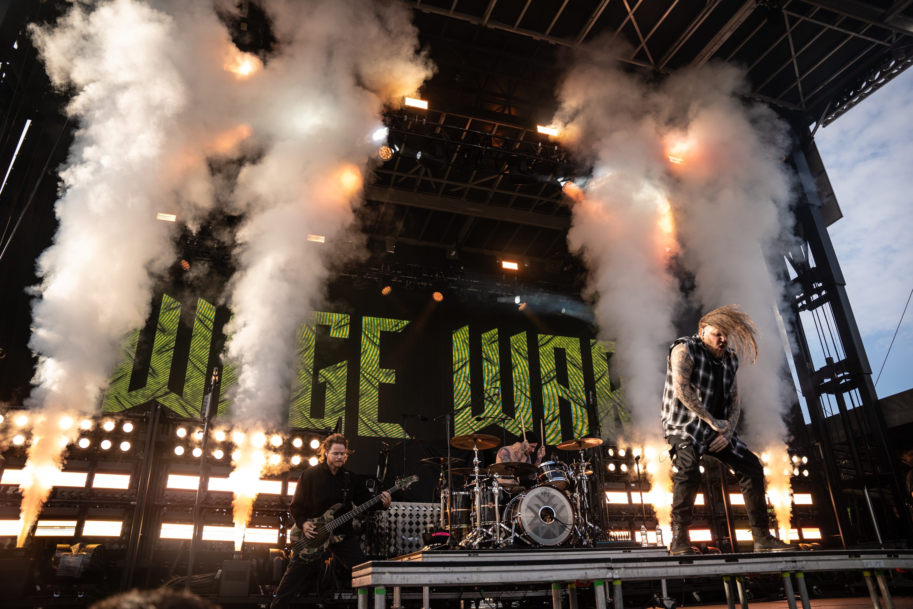 A live performance by the band Wage War with dramatic smoke effects on stage and vibrant lighting, showcasing the energetic atmosphere of a music festival.