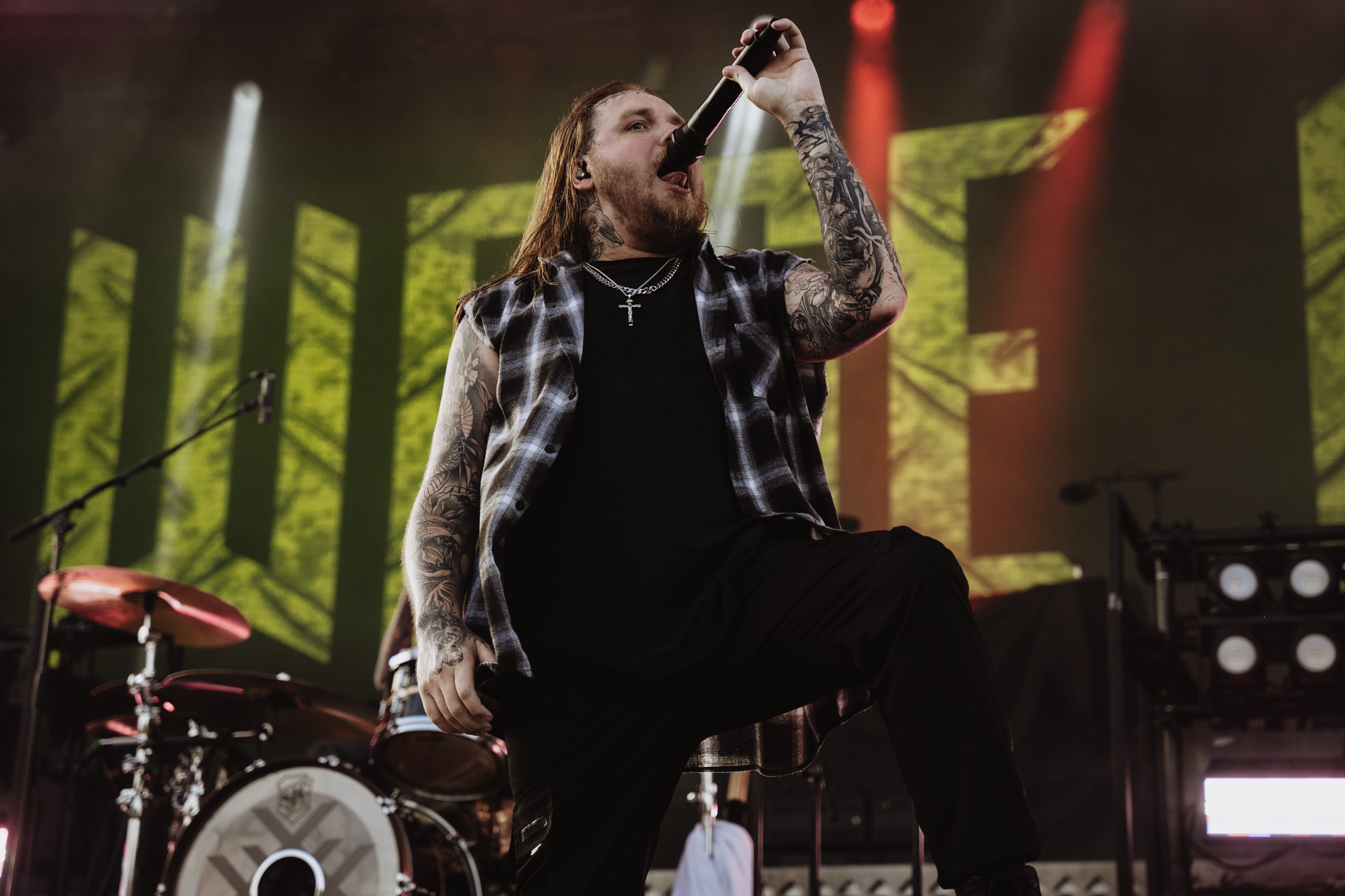 A vocalist passionately performing on stage during a music festival, with elaborate stage lighting and a large backdrop.