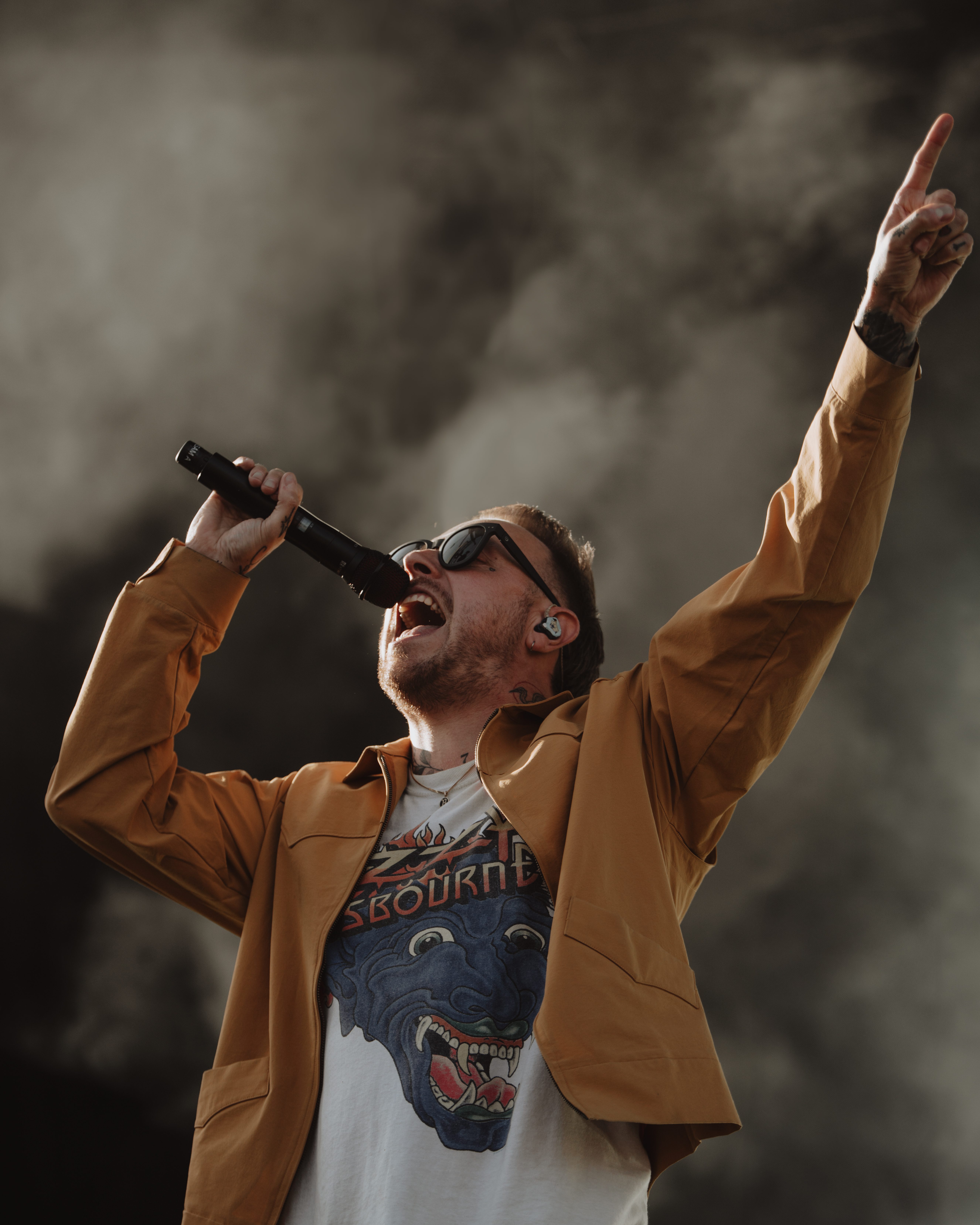 Close-up of a guitarist's hand playing an electric guitar, featuring a silver body and clear details of the player's tattoos and clothing.