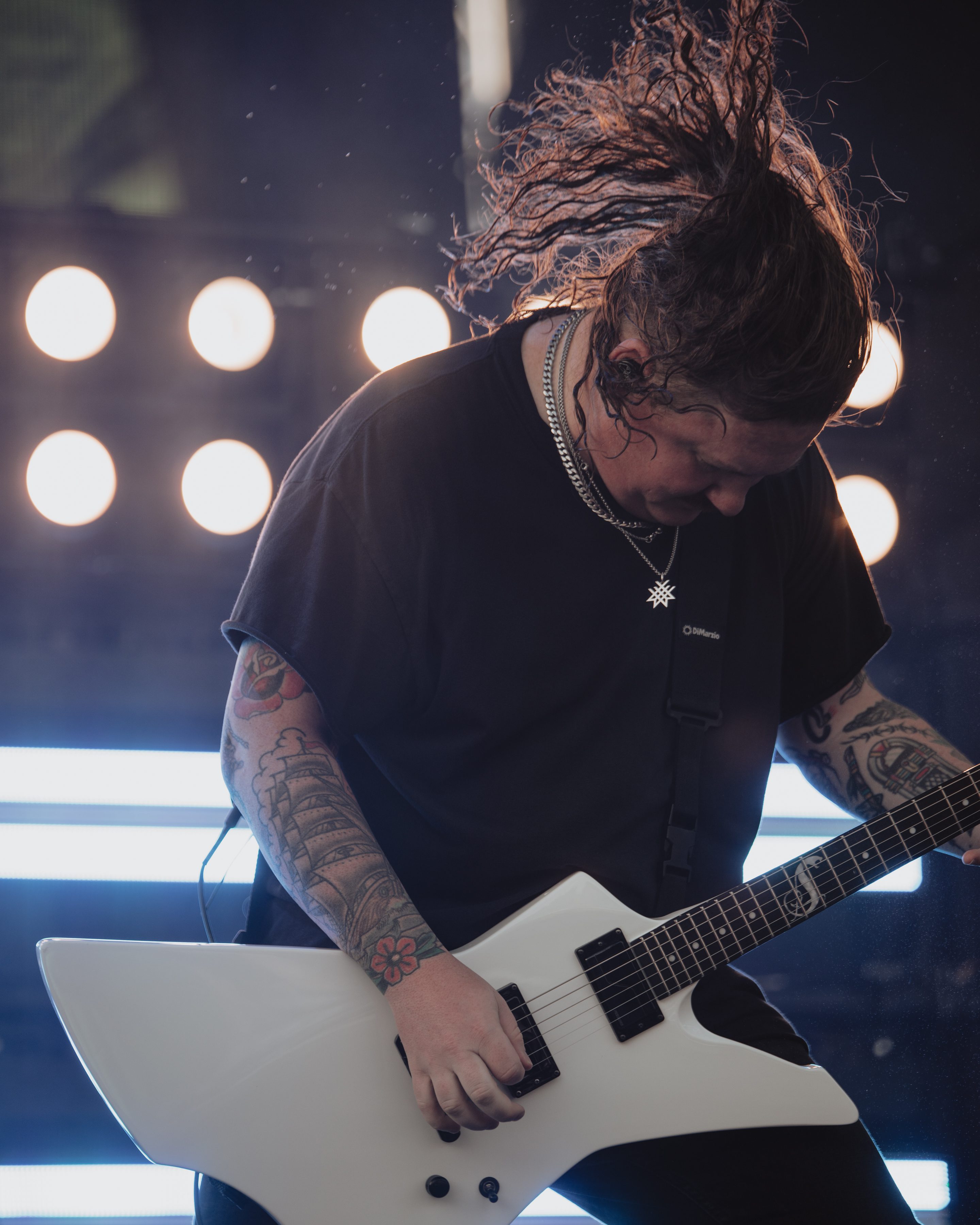 A guitarist passionately playing an electric guitar with long, curly hair flying as he focuses on his performance, surrounded by bright stage lights.