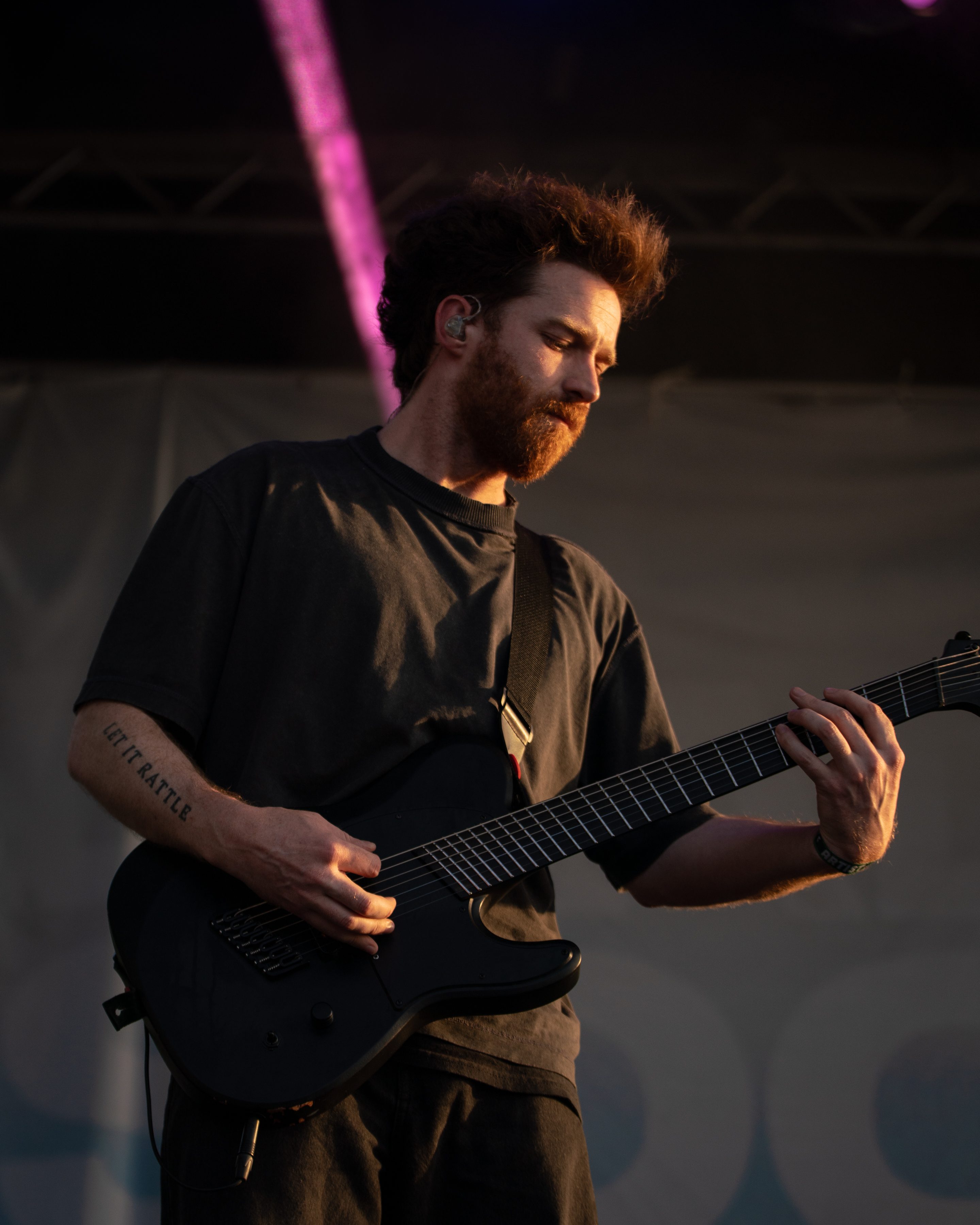 A guitarist performing on stage with a serious expression, wearing a dark t-shirt, and showcasing his skill on a black electric guitar.