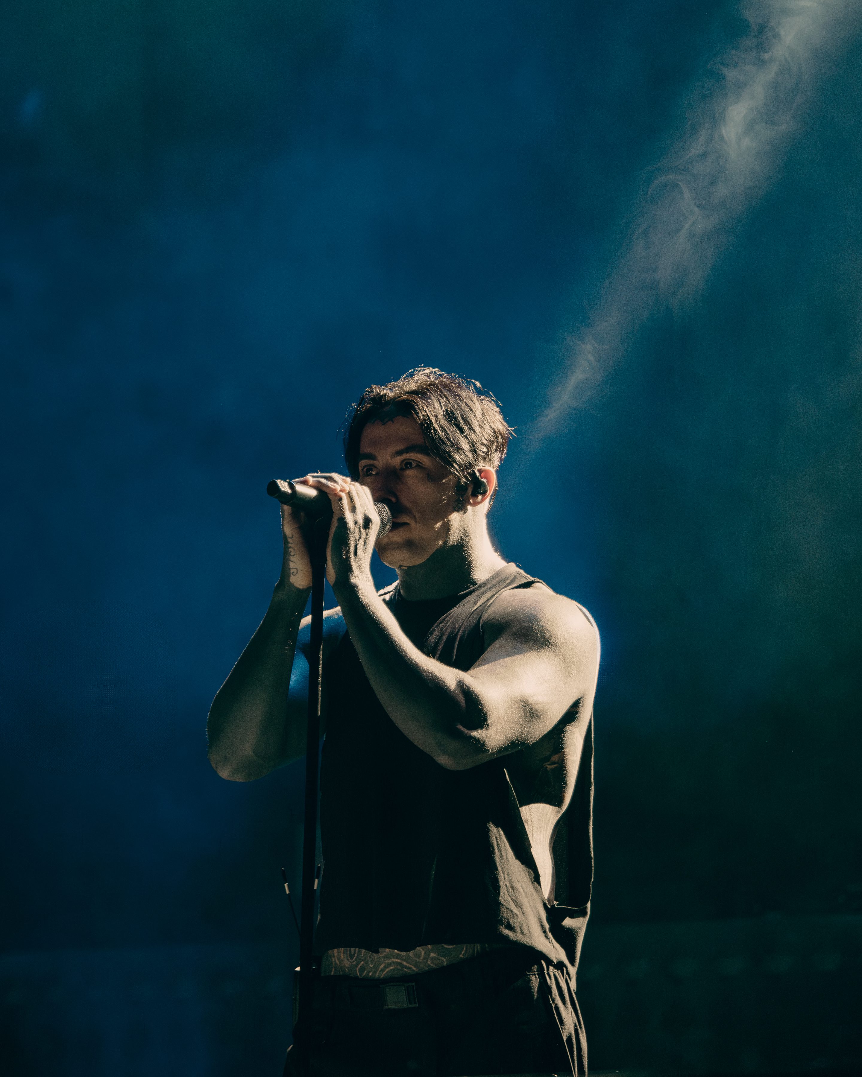 A male singer performing on stage with a microphone, surrounded by blue lighting and a smoky atmosphere.