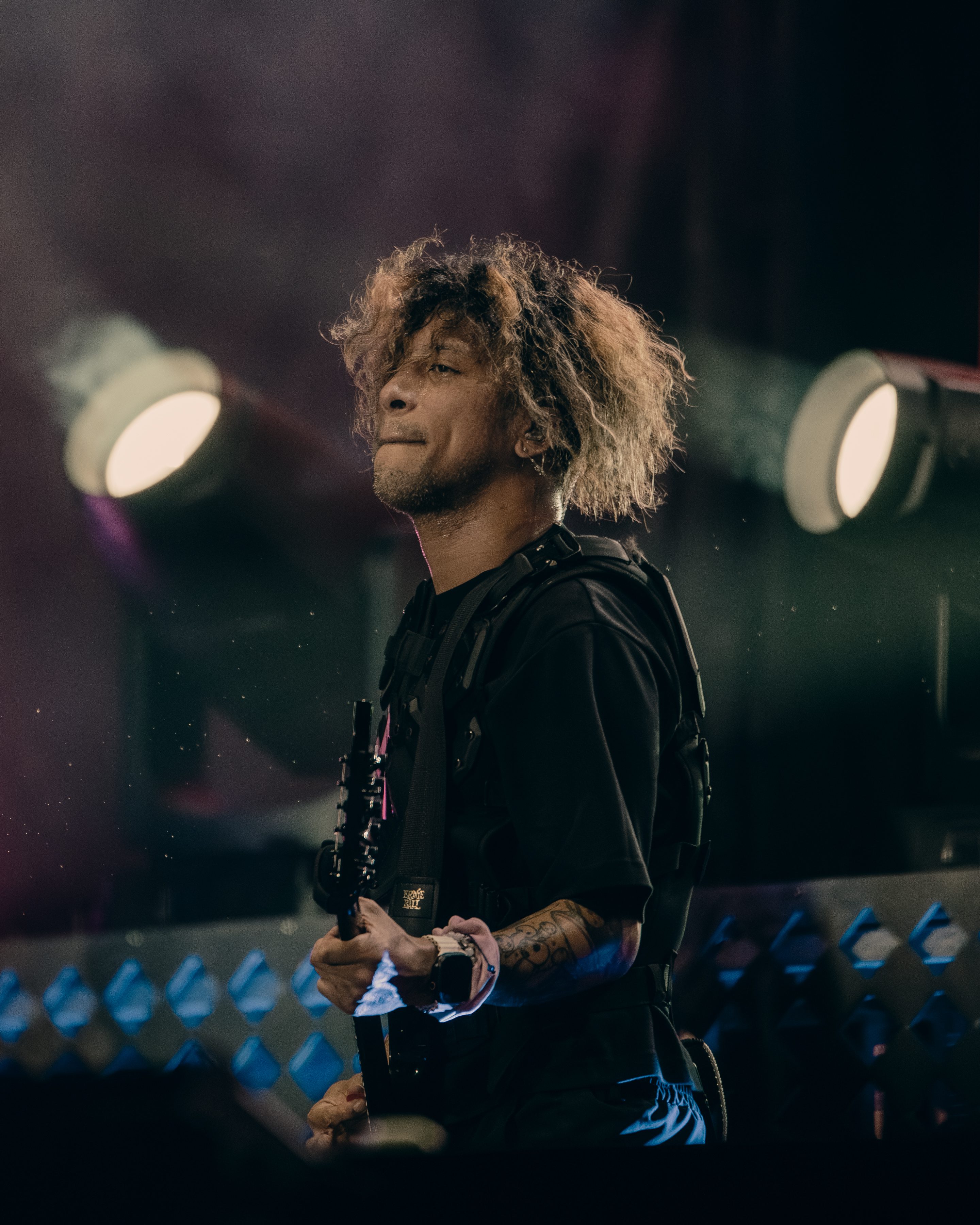 A musician performing on stage, playing an electric guitar with a focused expression, surrounded by vibrant stage lights and smoke effects.
