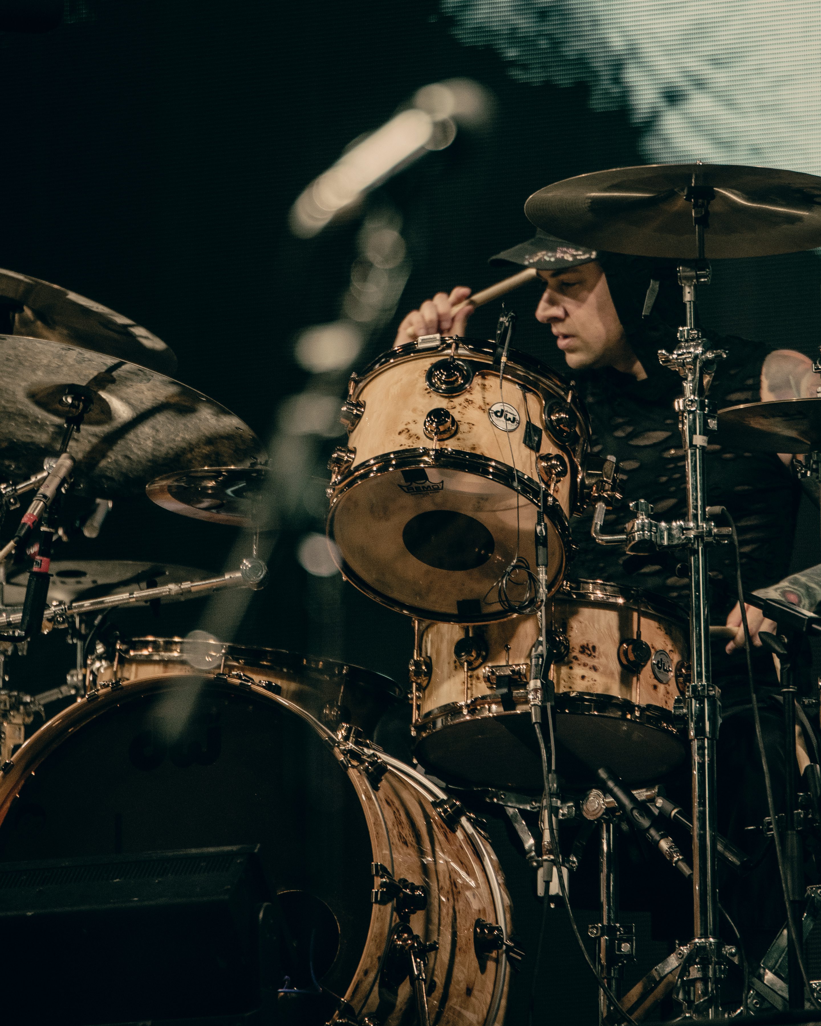 A drummer playing an elaborate drum set with a focused expression during a live performance.