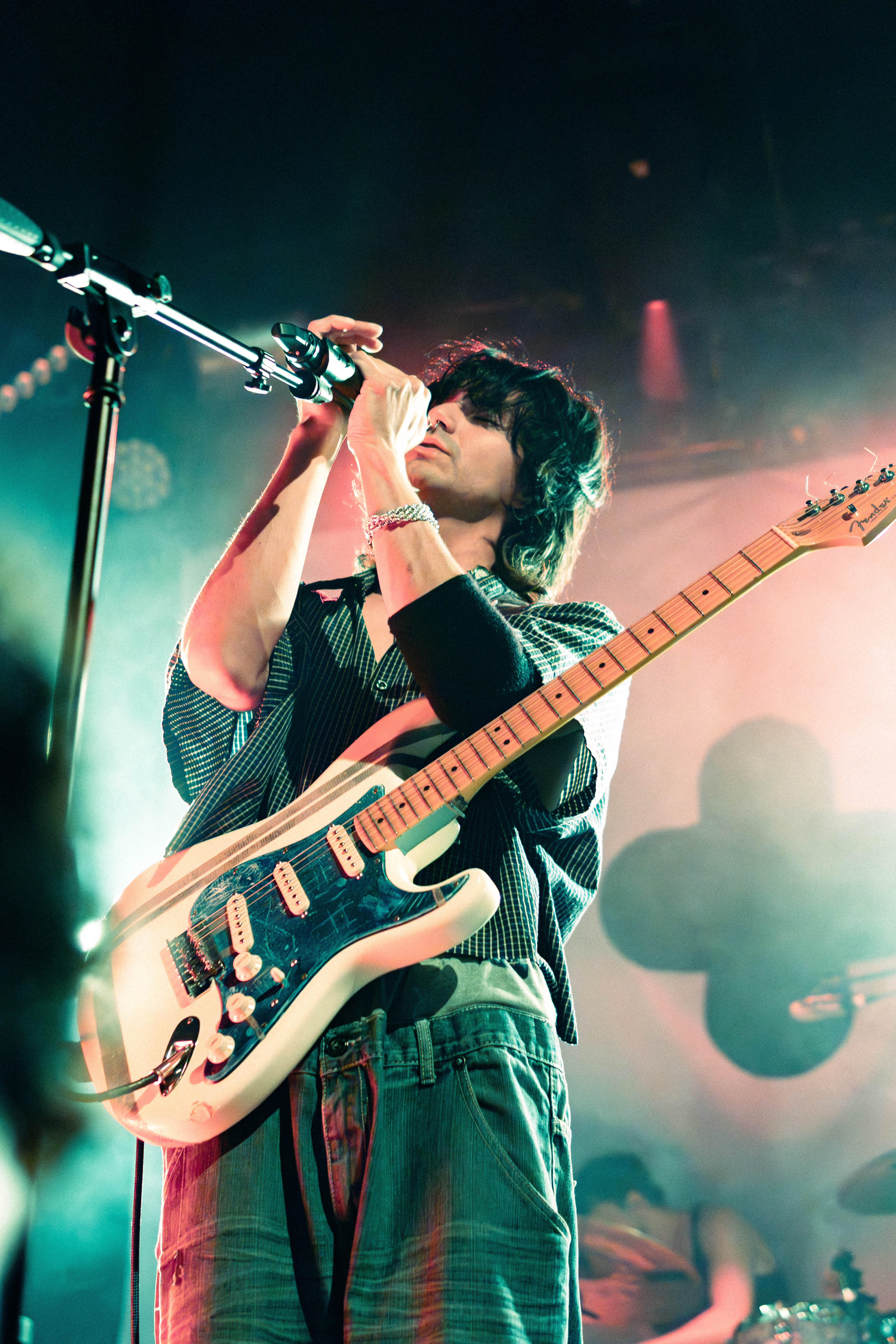 A musician performing on stage, holding a microphone and guitar, with colorful stage lights in the background.