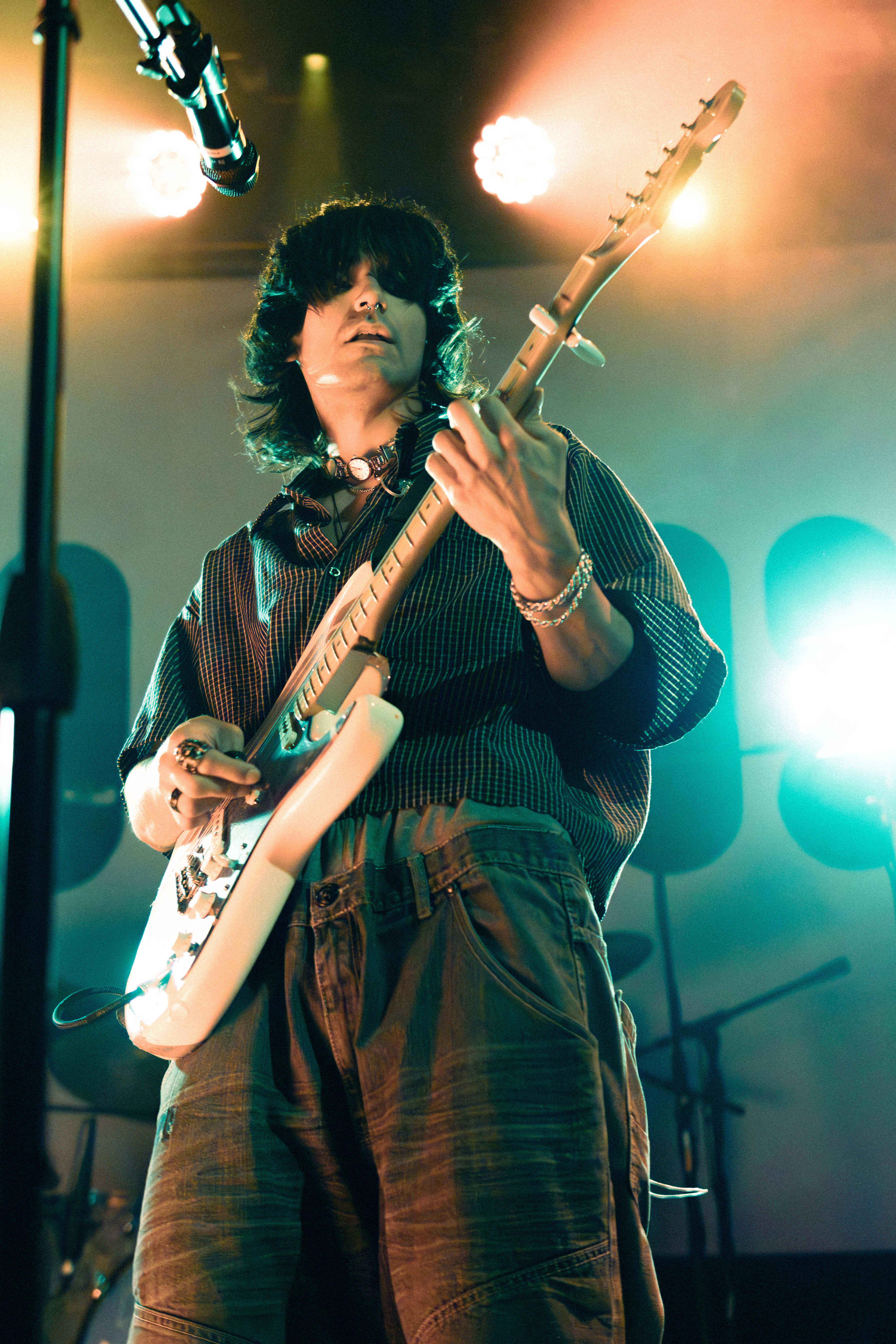 A musician performing live on stage, playing an electric guitar under vibrant stage lights, with a focus on their energetic expression.