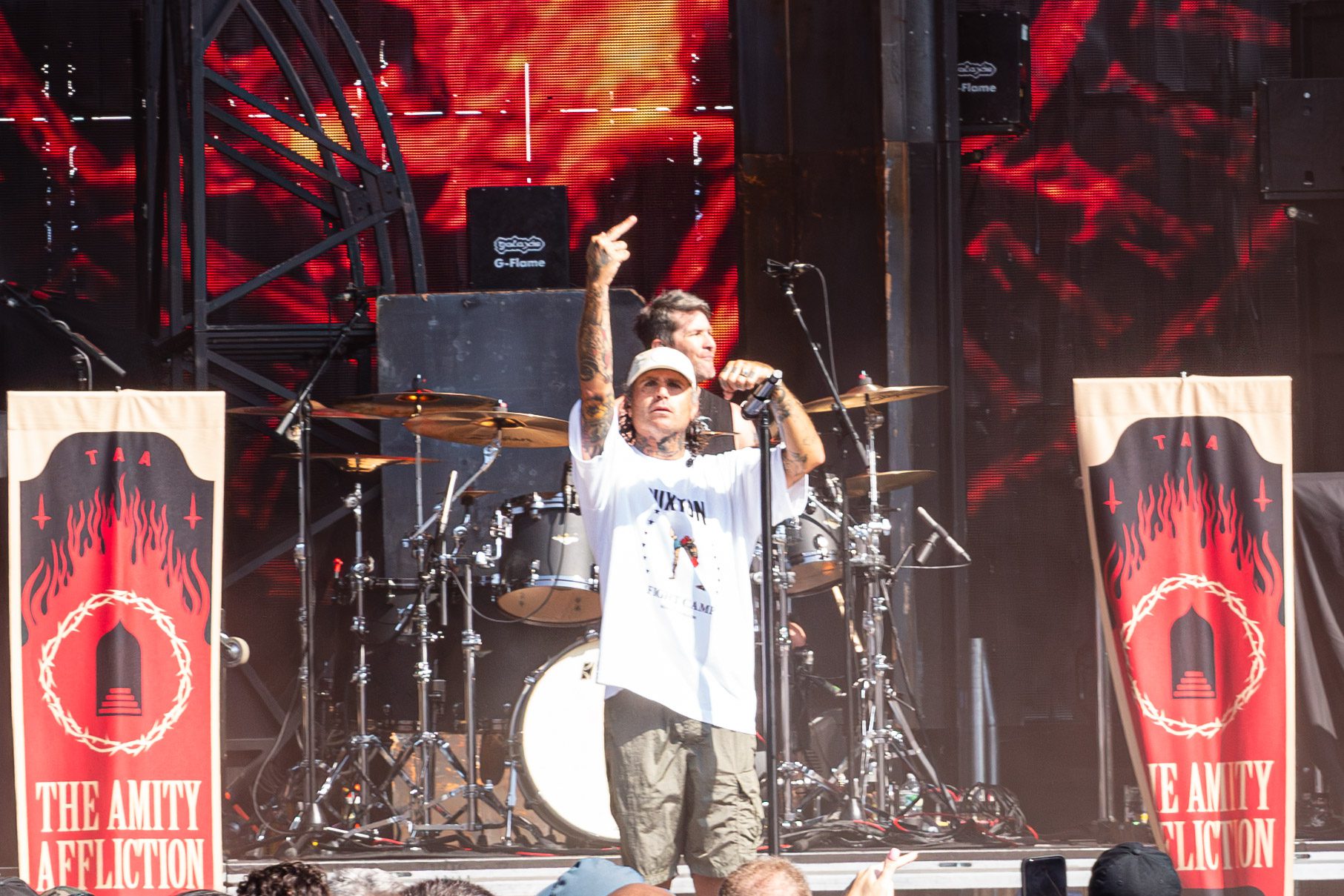 Lead vocalist performing on stage at a music festival with a drum set in the background and banners featuring the band's logo.