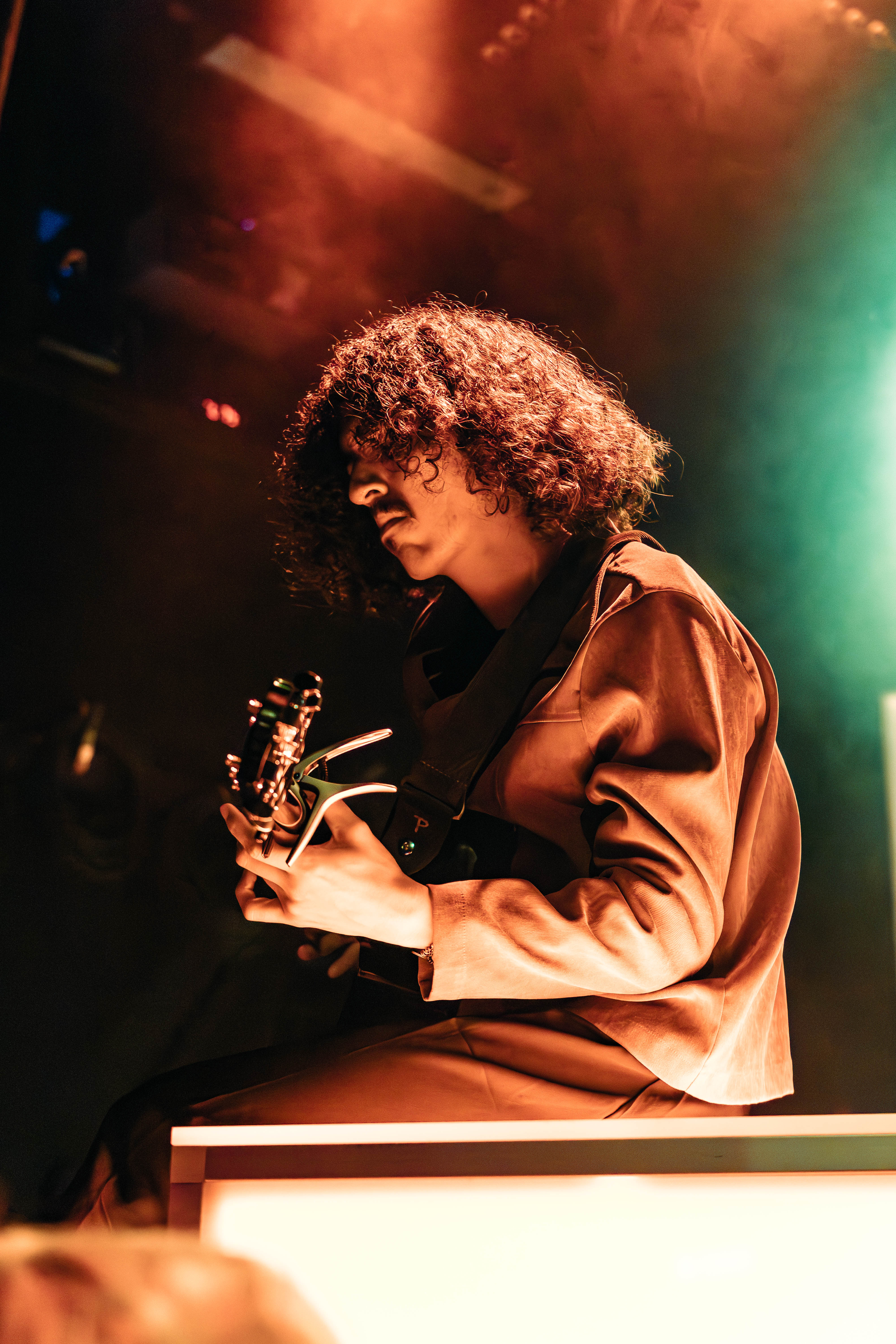 A musician with curly hair plays guitar on stage, surrounded by atmospheric lighting.