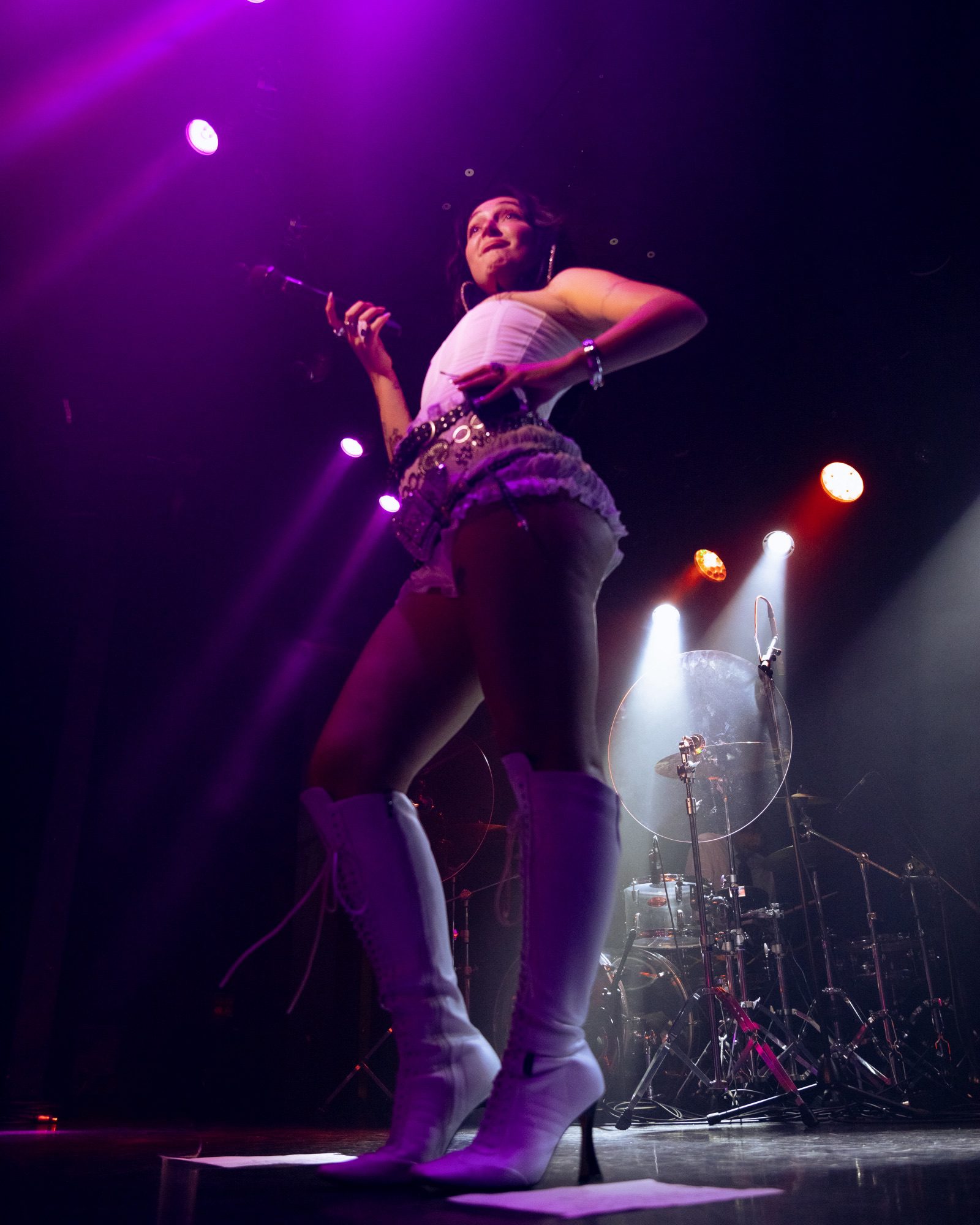 Singer Cil performing on stage in a chic outfit with knee-high white boots, holding a microphone under purple stage lights.