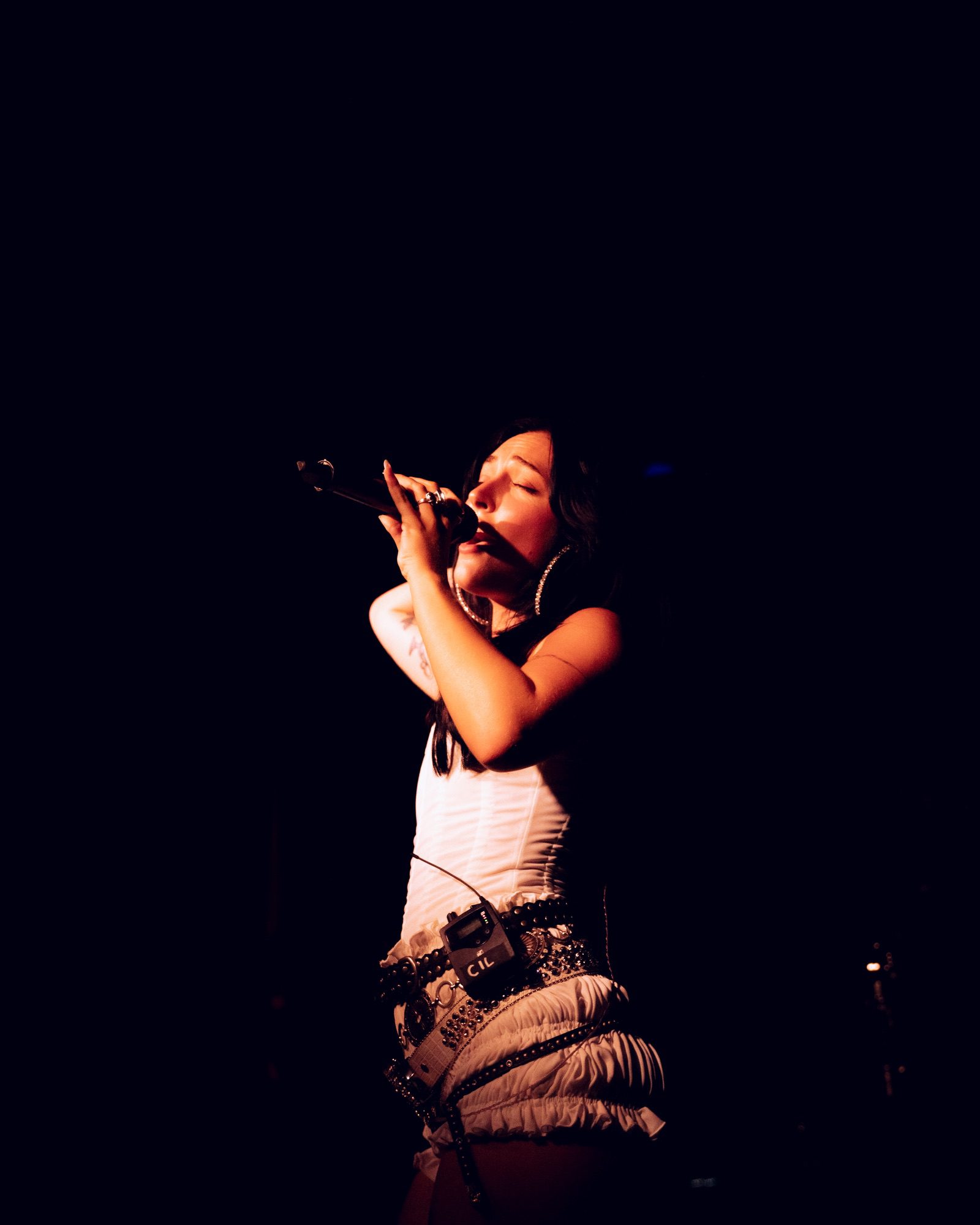 Rising pop star Cil performing on stage, singing passionately into a microphone, illuminated by stage lights.