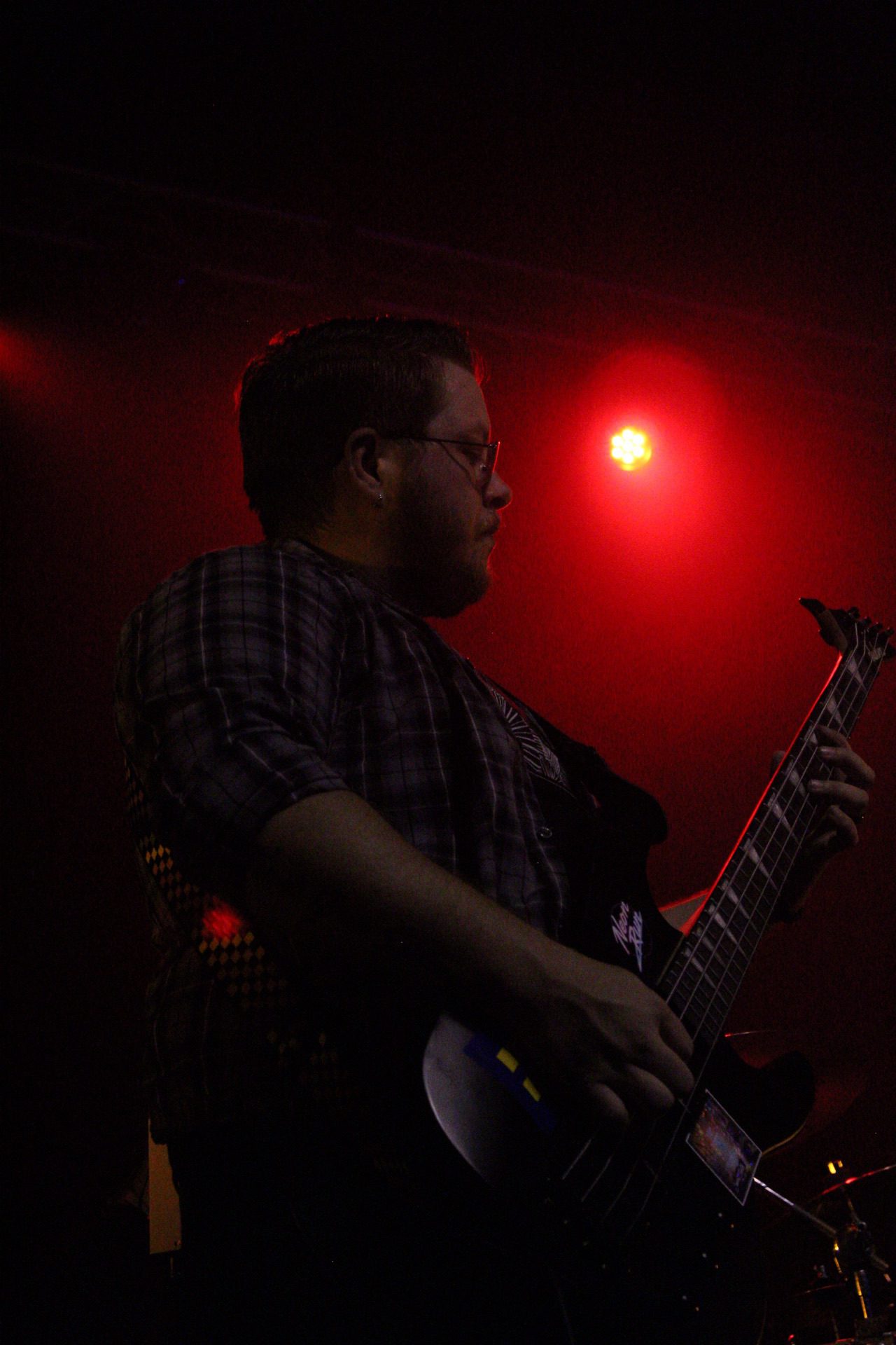 A musician playing bass guitar on stage with red lighting in the background.