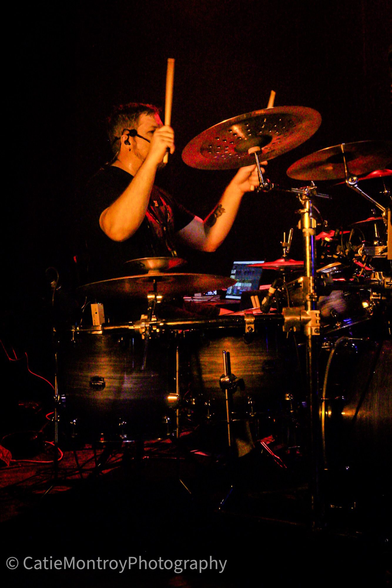 A drummer playing passionately on stage, surrounded by drums and cymbals, with dramatic lighting enhancing the atmosphere.