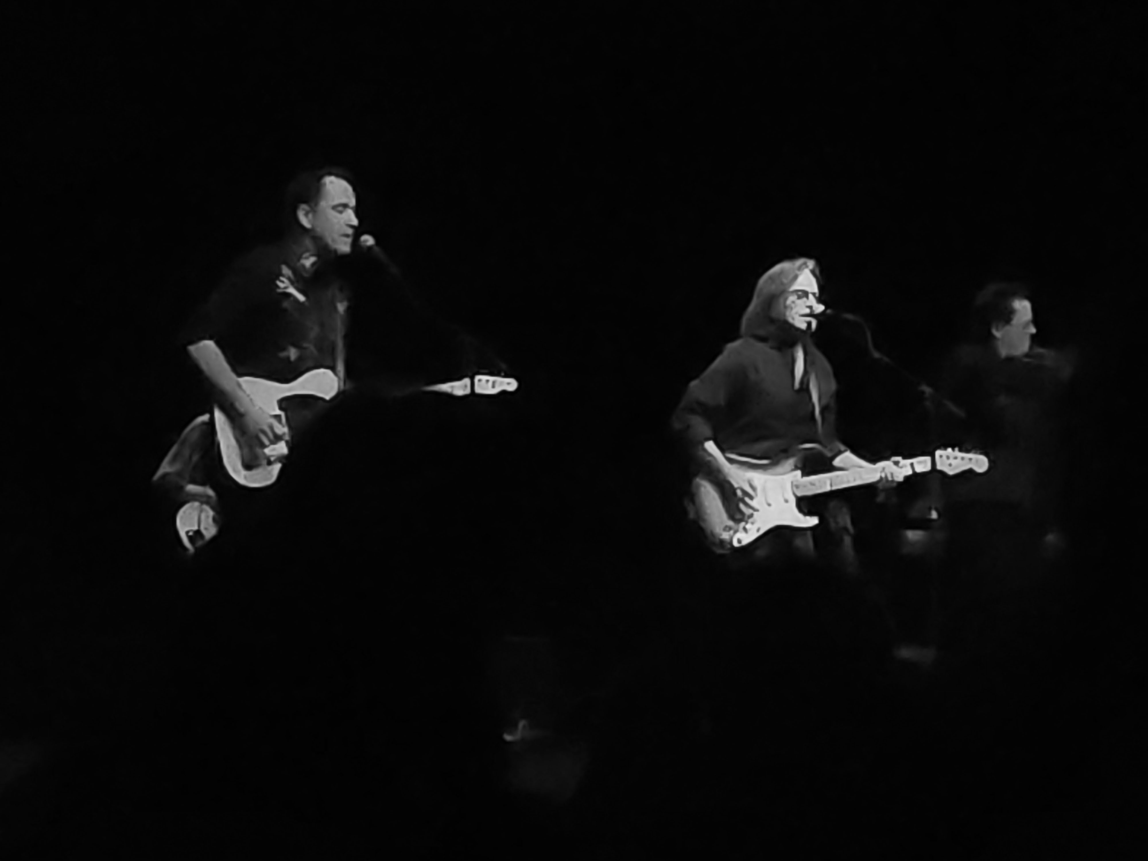 Two musicians performing on stage at a concert, one playing guitar and singing into a microphone.