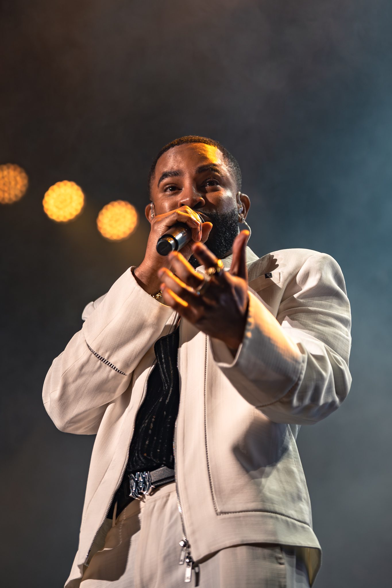Elijah Blake performing on stage, wearing a light-colored outfit and holding a microphone while engaging with the audience.