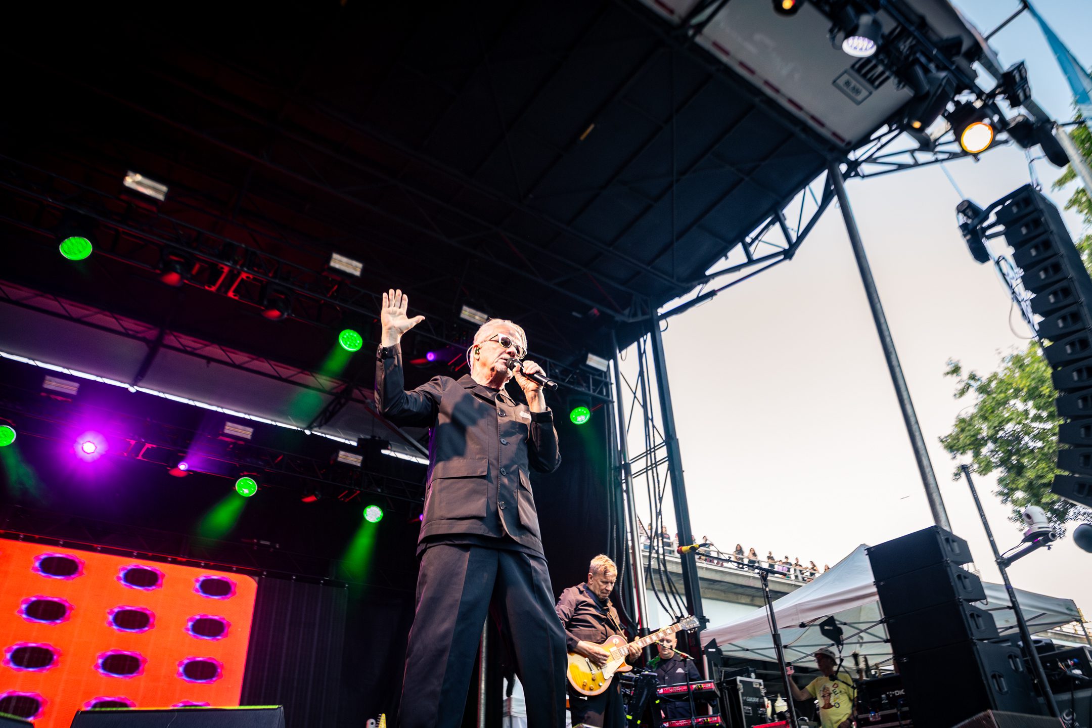 A singer performing on stage during a lively concert, gesturing to the audience, with vibrant lights illuminating the backdrop.