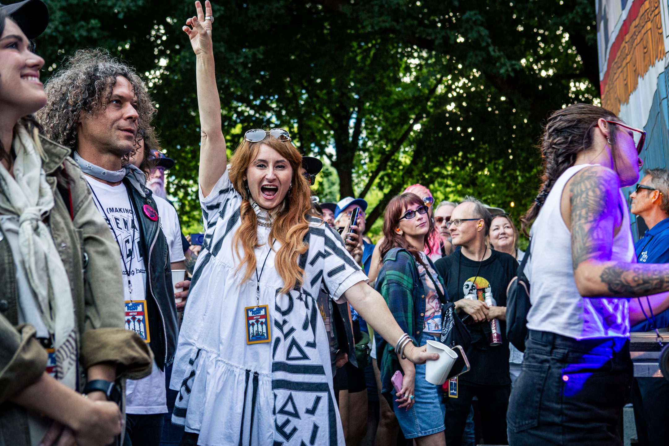 A lively crowd at a music festival, with a woman in a white dress joyfully raising her arm in celebration, surrounded by excited attendees enjoying the performance.