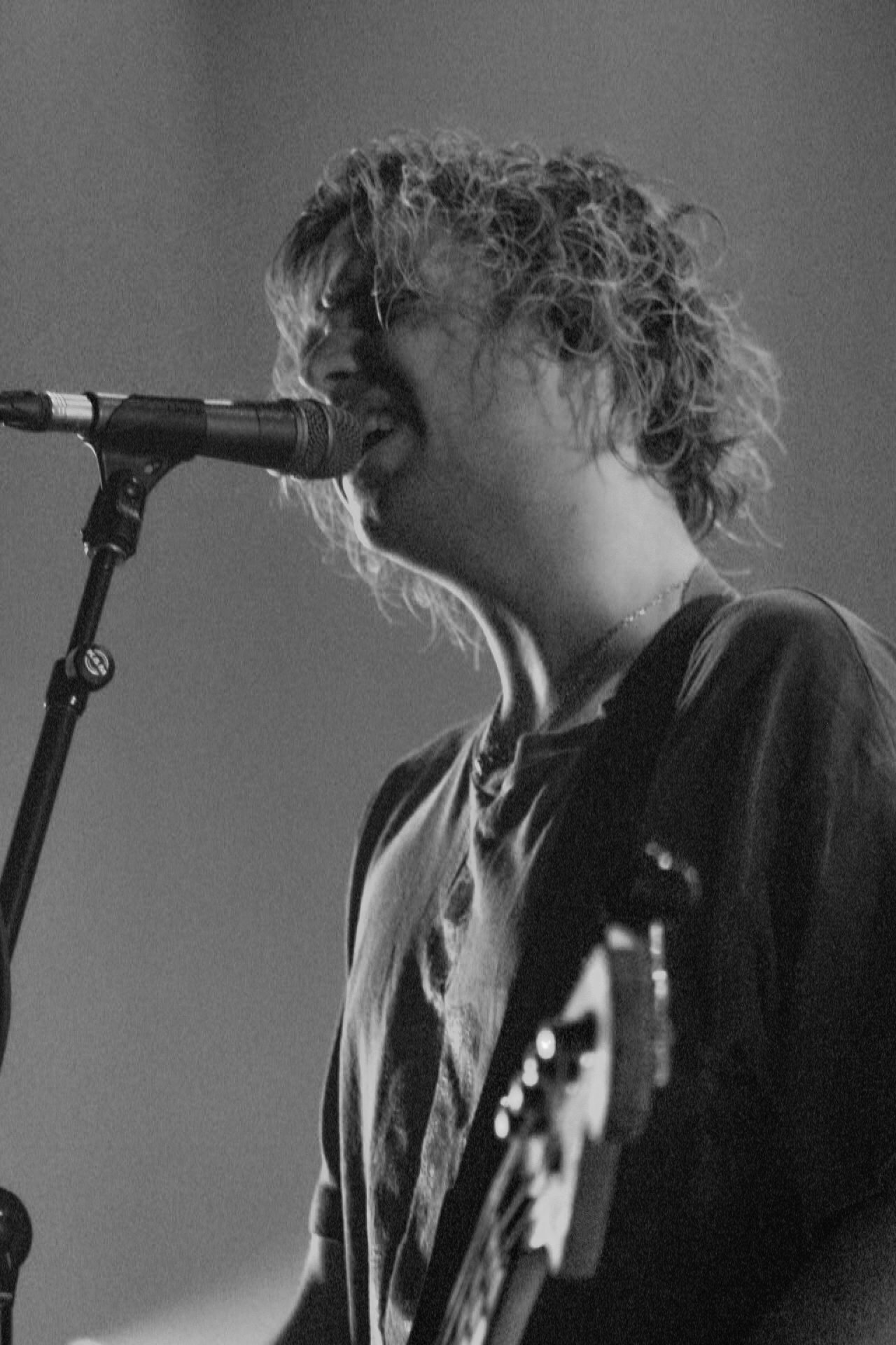 A lead singer passionately performing into a microphone during a live concert, captured in black and white.