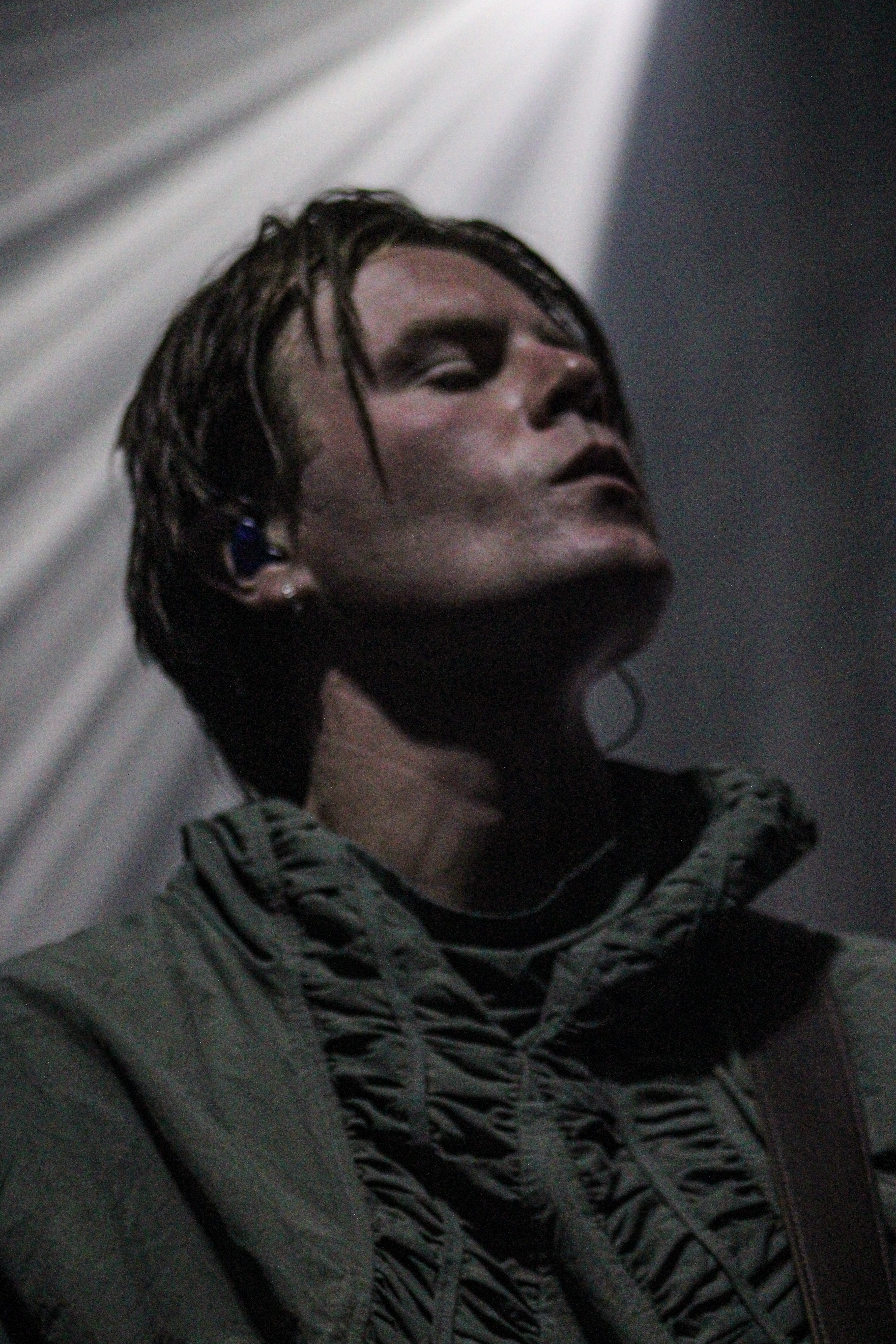 Close-up of a male musician with long hair, wearing a green jacket, performing on stage with dramatic lighting in the background.