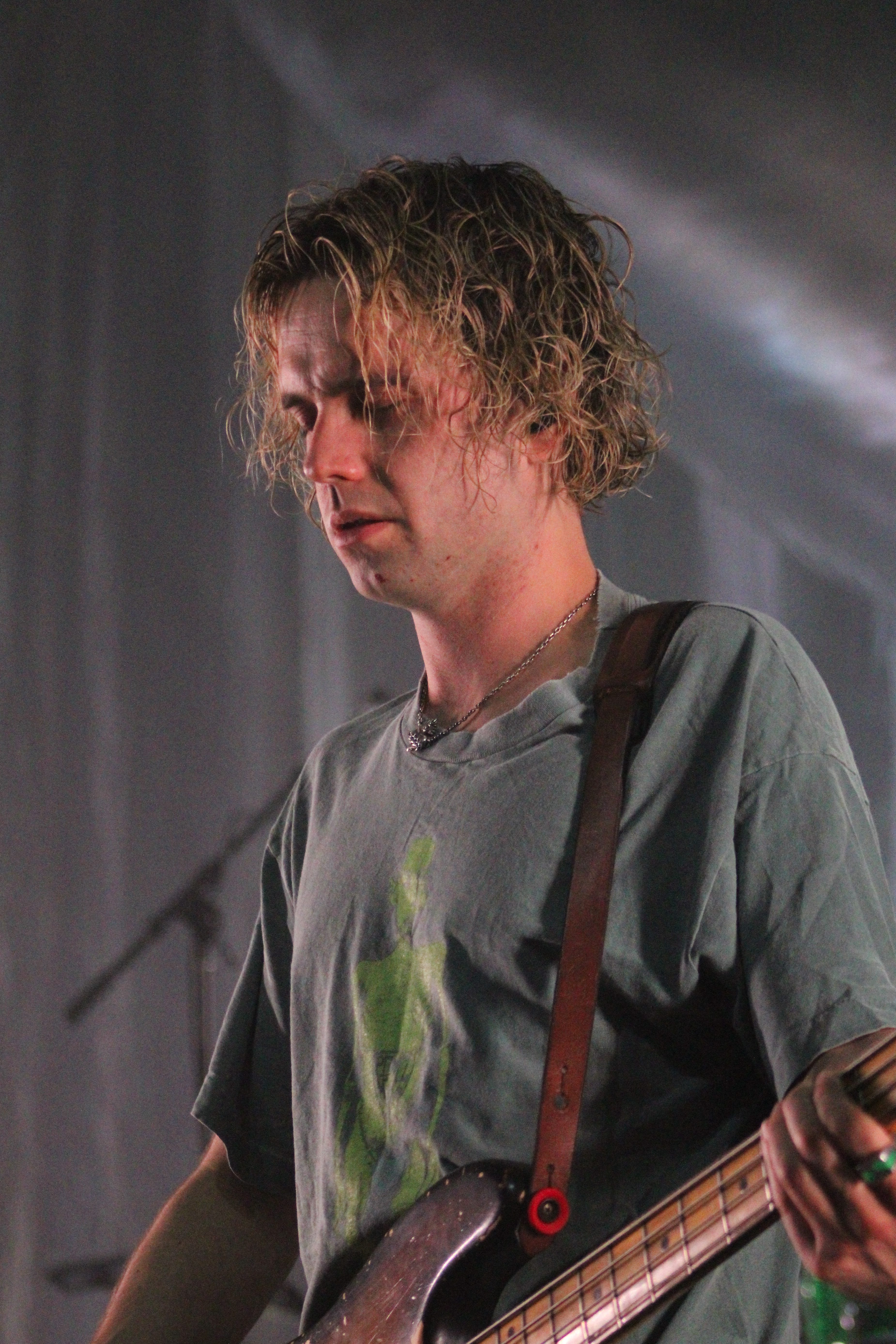 A musician from the Irish rock band Fontaines D.C. performs on stage, displaying deep concentration while playing the bass guitar.