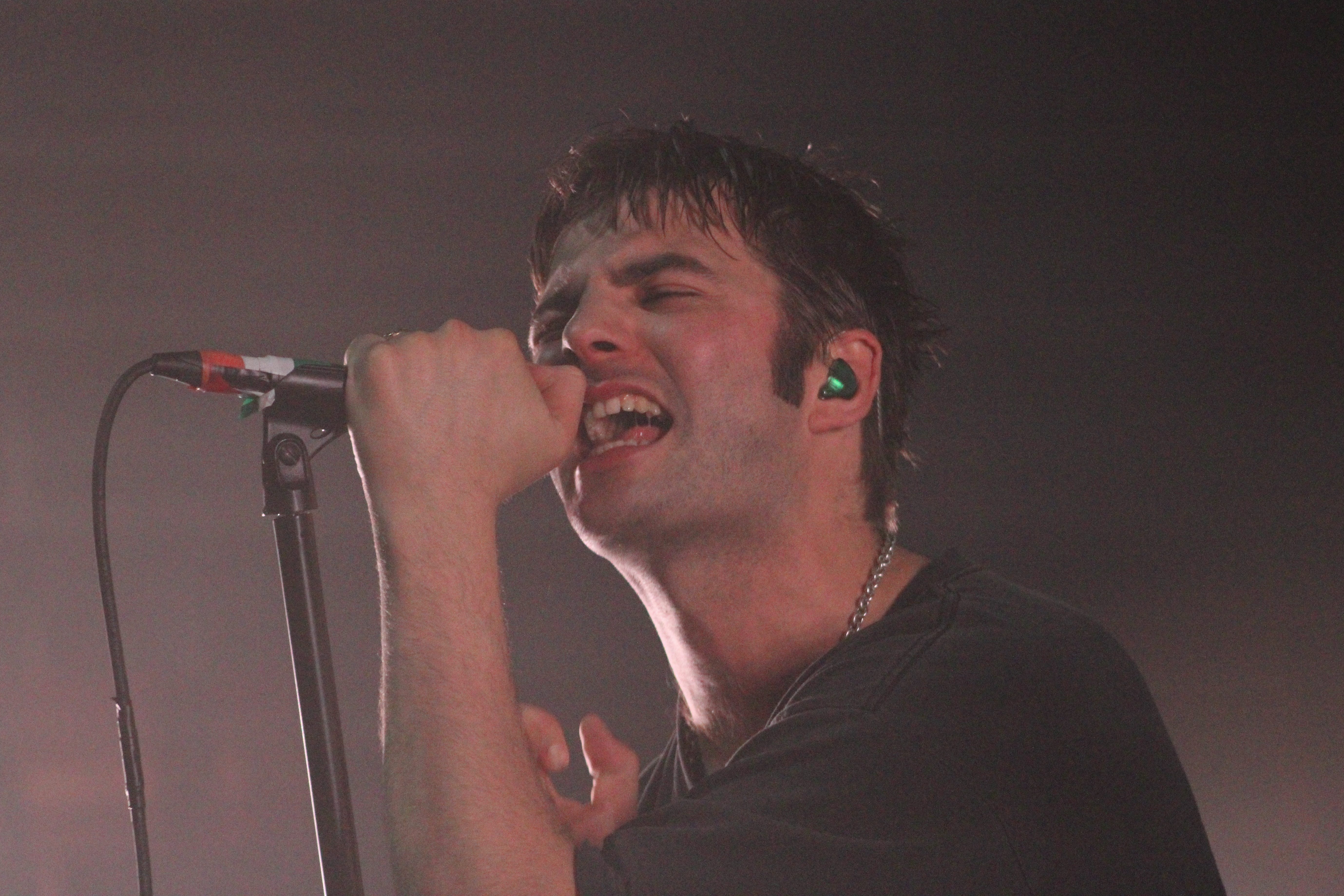 Close-up of a male singer passionately performing on stage, gripping a microphone, with intense facial expression and stage lighting in the background.