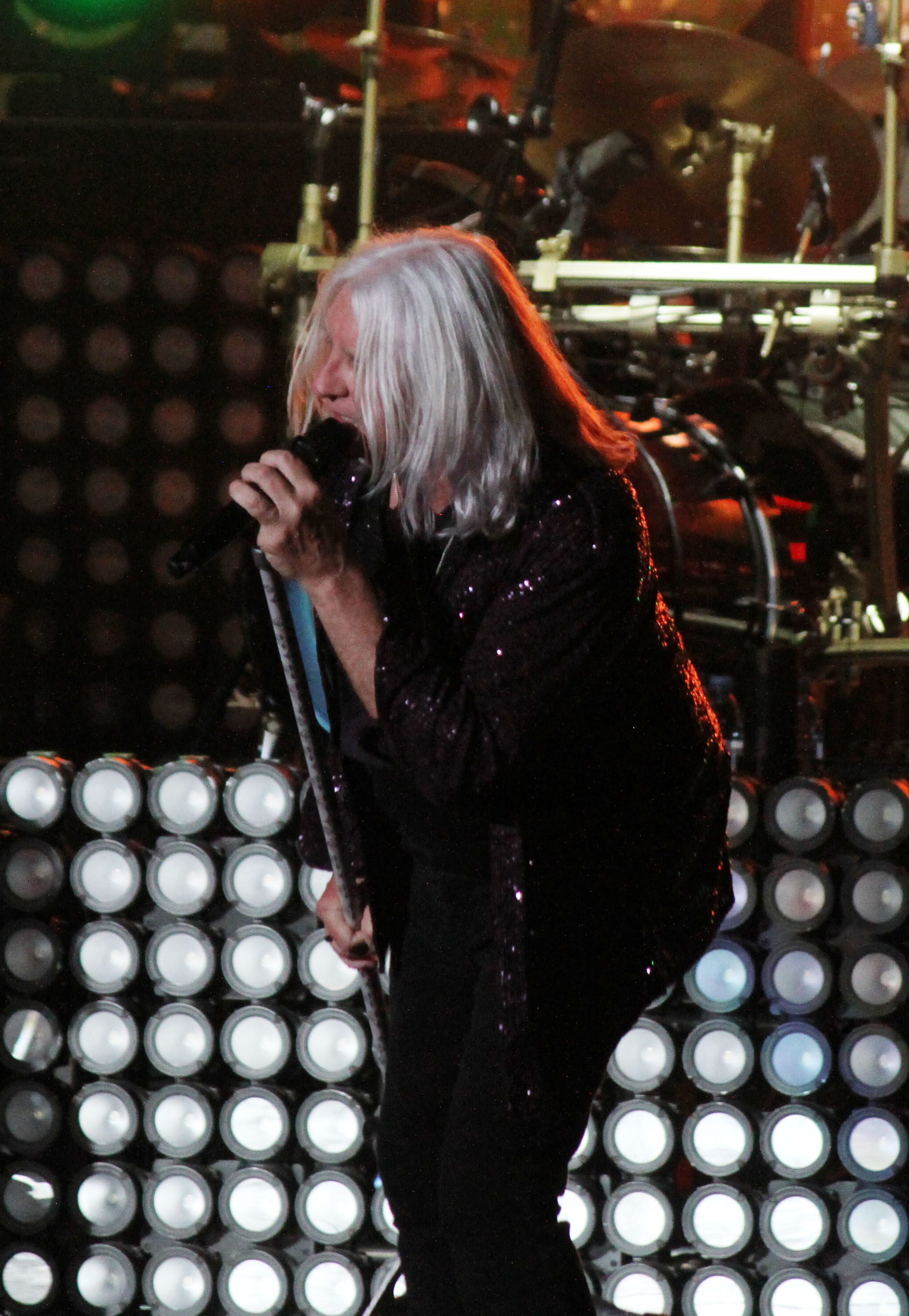 A lead singer performs passionately on stage during a concert, illuminated by vibrant stage lights, with a backdrop of circular lights.