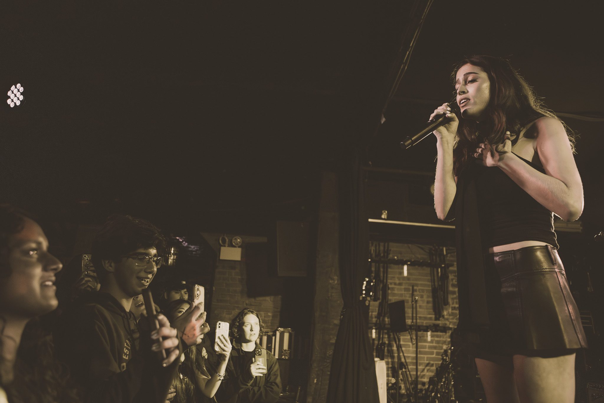 A singer performing passionately on stage, engaging with an audience holding smartphones to capture the moment.