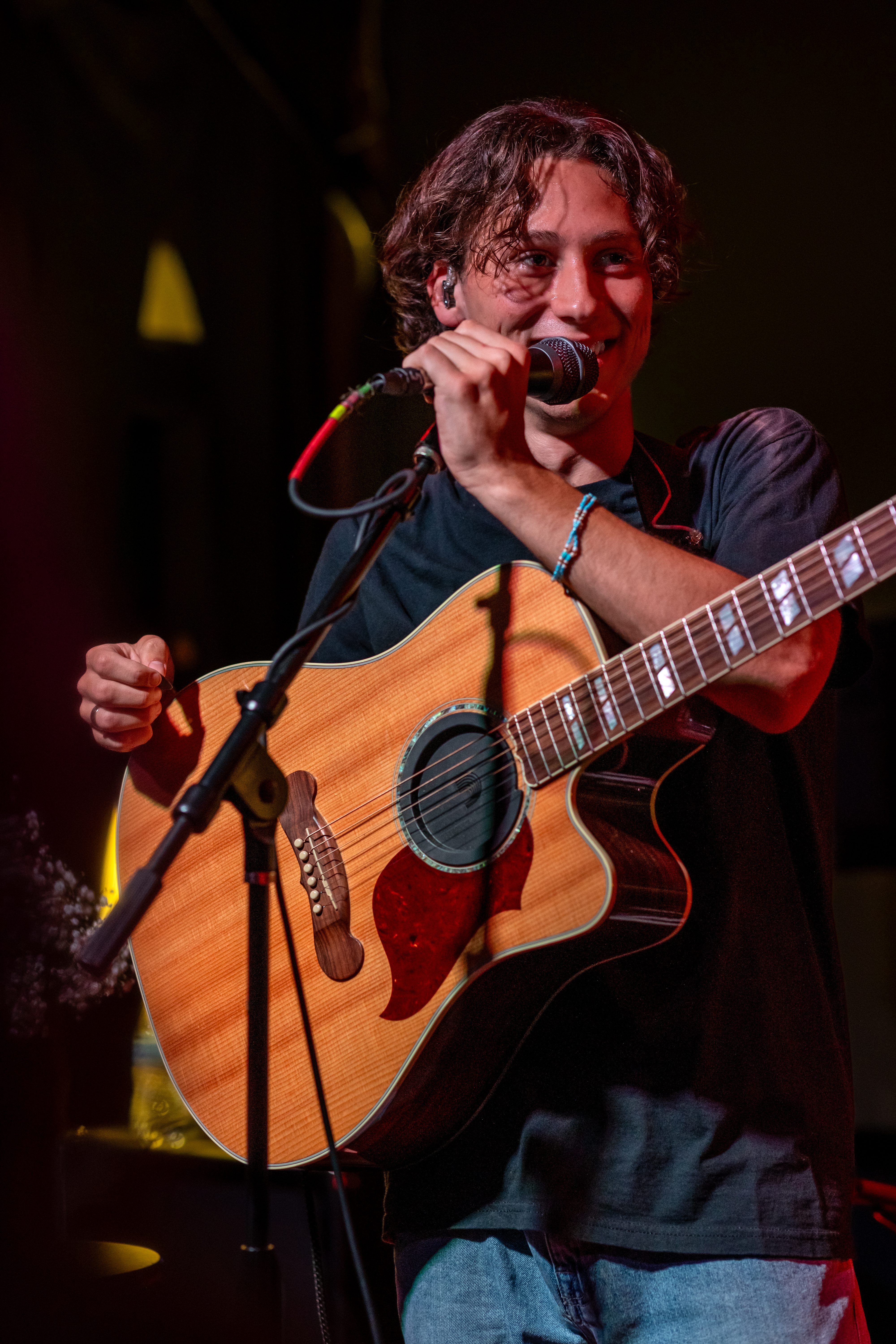 A musician smiling while holding an acoustic guitar and microphone during a performance.