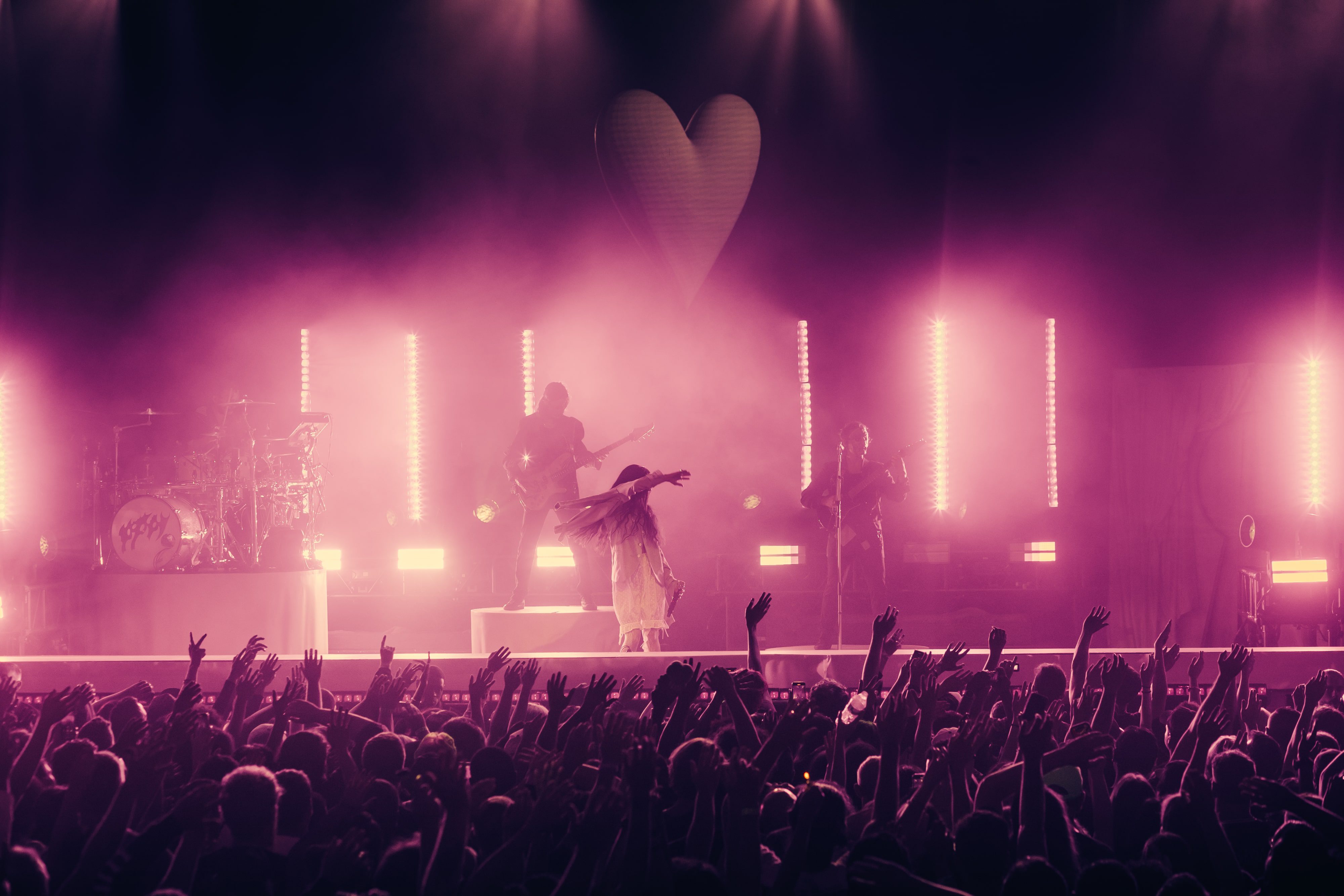 Poppy performs on stage with a vibrant light show, surrounded by an energetic crowd raising their hands.