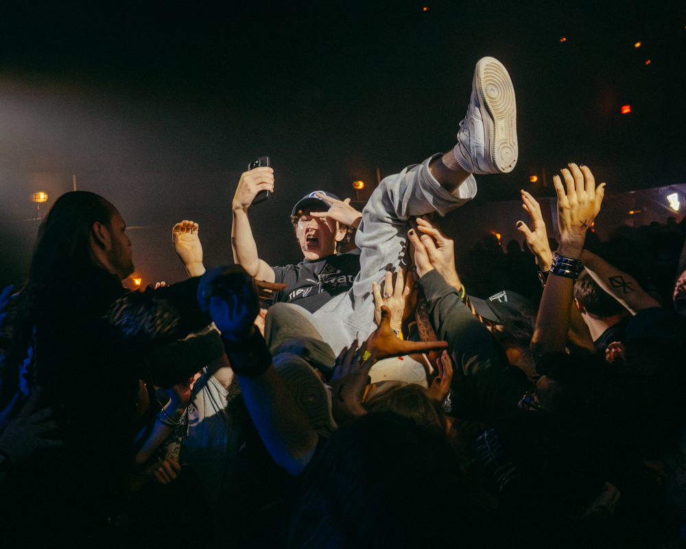 A crowd at a concert with a crowd-surfer being held up by enthusiastic fans, showcasing the lively atmosphere of a music performance.