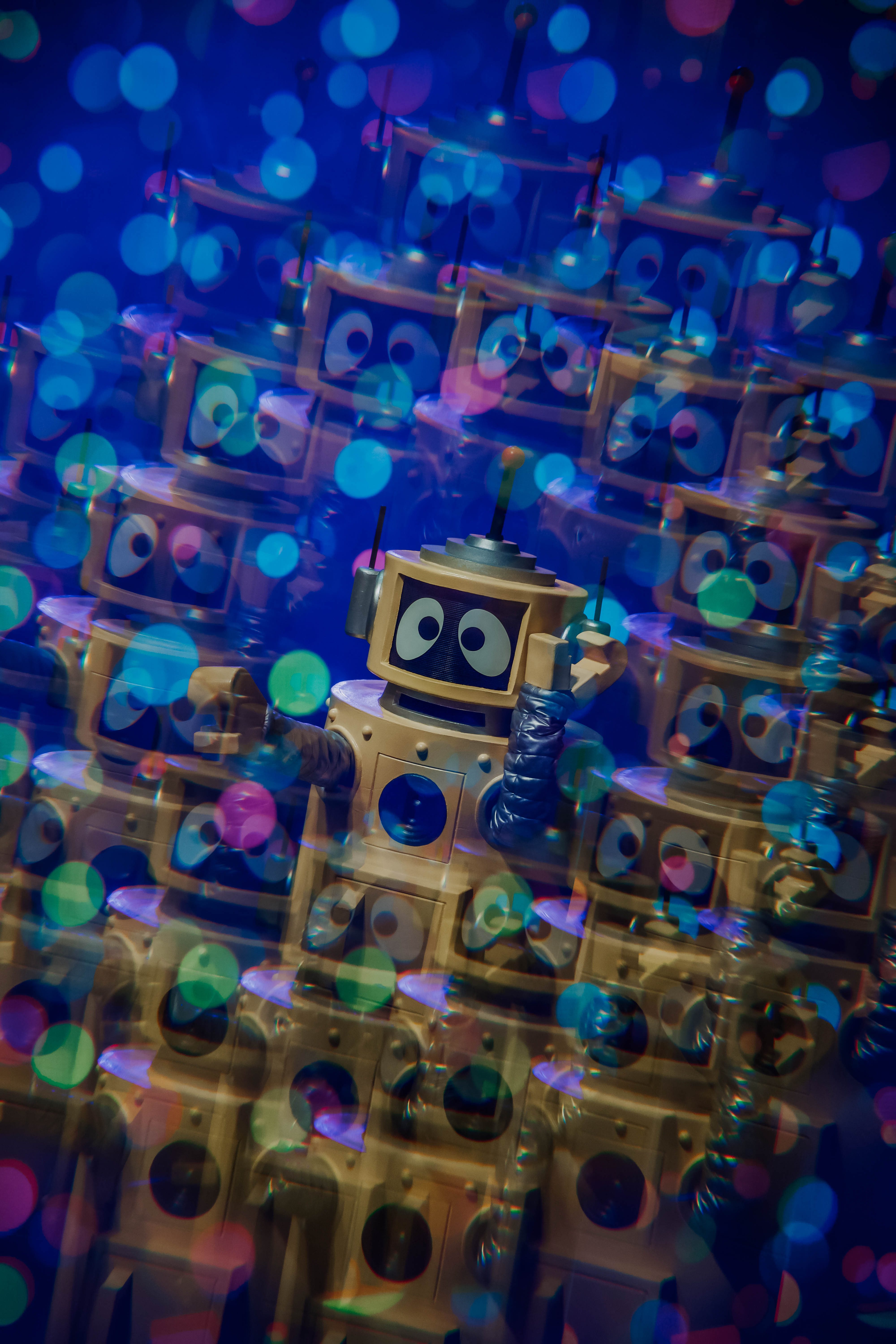 A cheerful robot character with large eyes amidst a colorful backdrop of blurred circles, resembling a festive atmosphere.