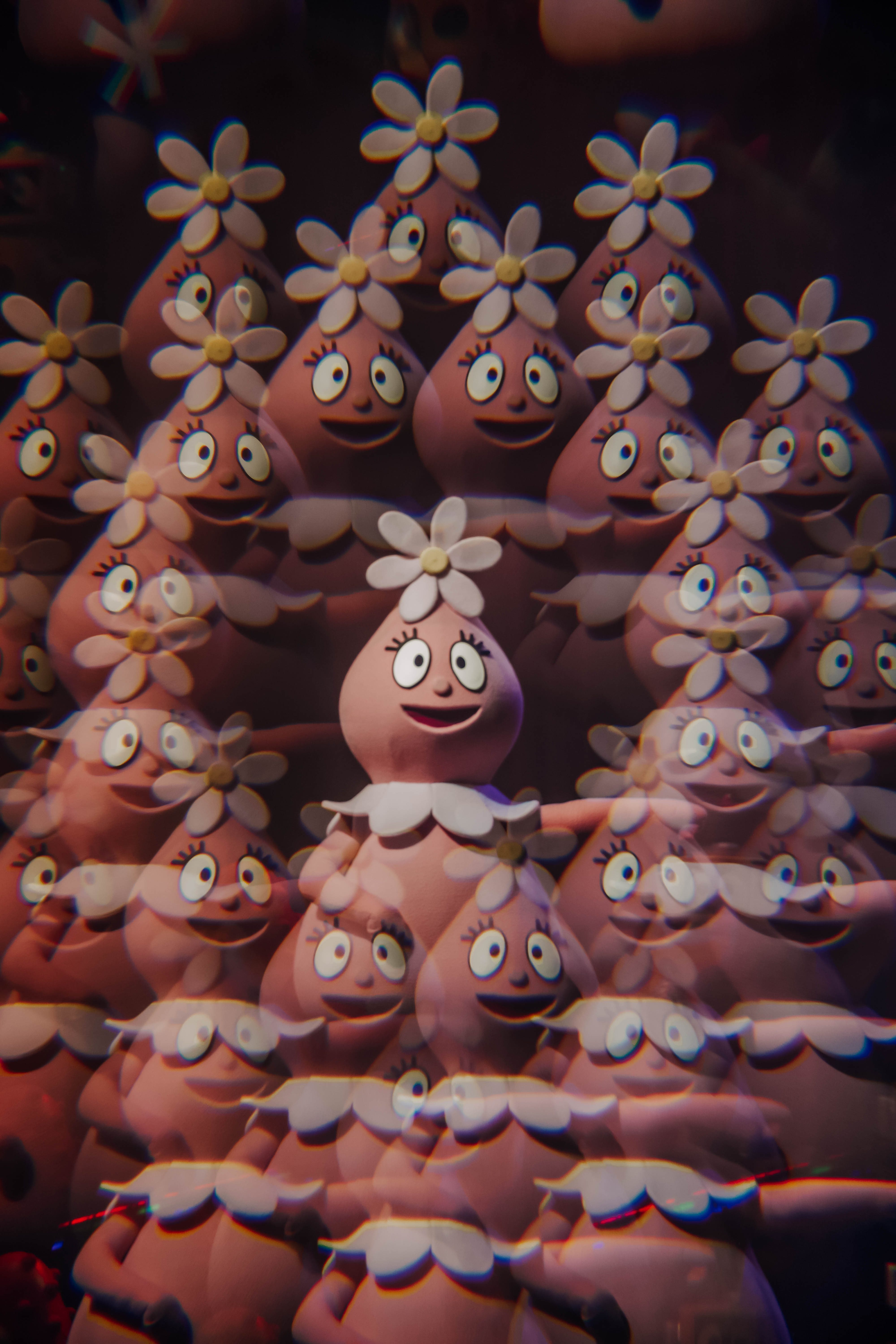 A colorful display of multiple character figures from the show, featuring a pink character with a flower on its head and a cheerful expression, surrounded by other similar characters.