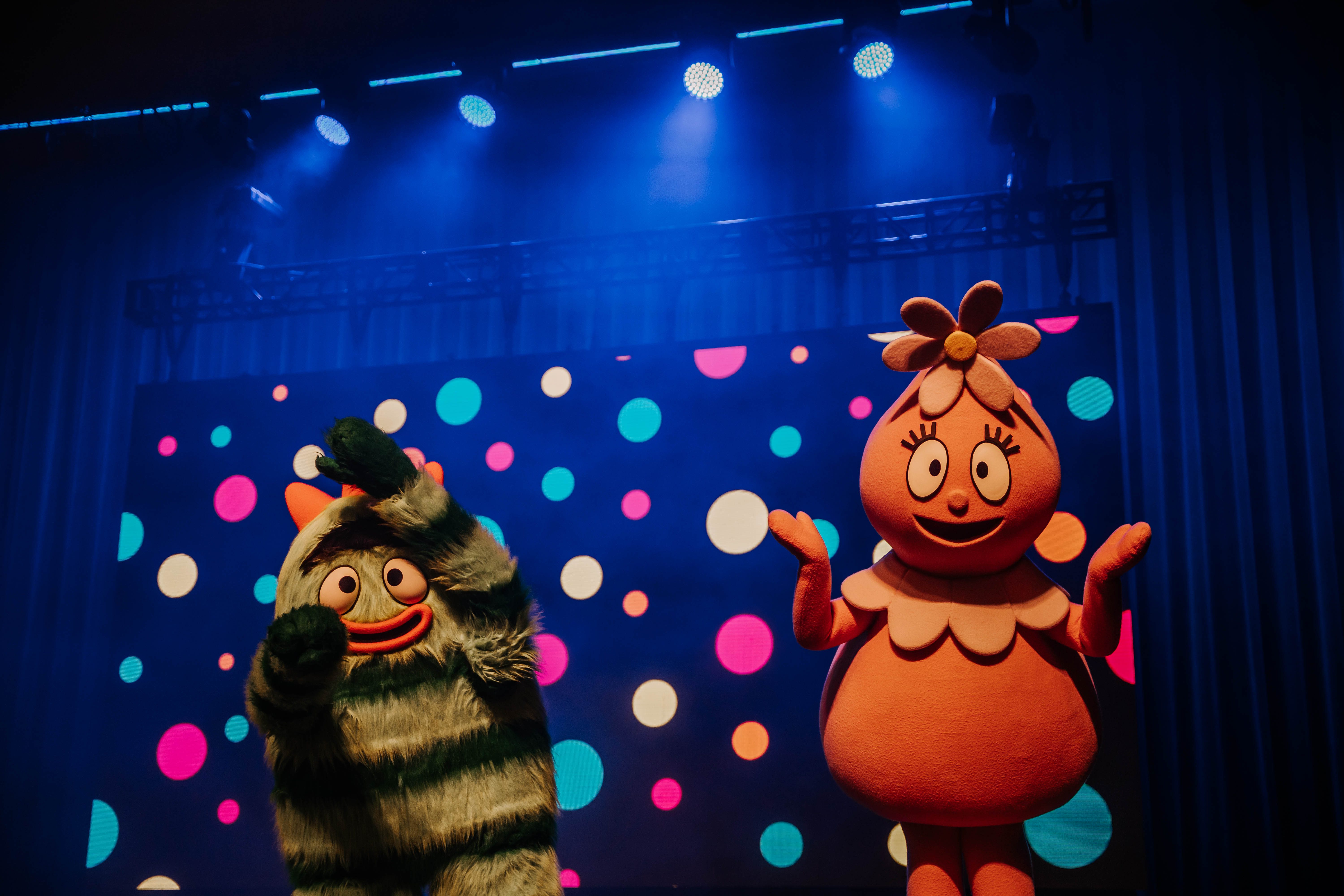 Two colorful characters from _Yo Gabba Gabba!_ performing on stage with a vibrant backdrop of polka dots.