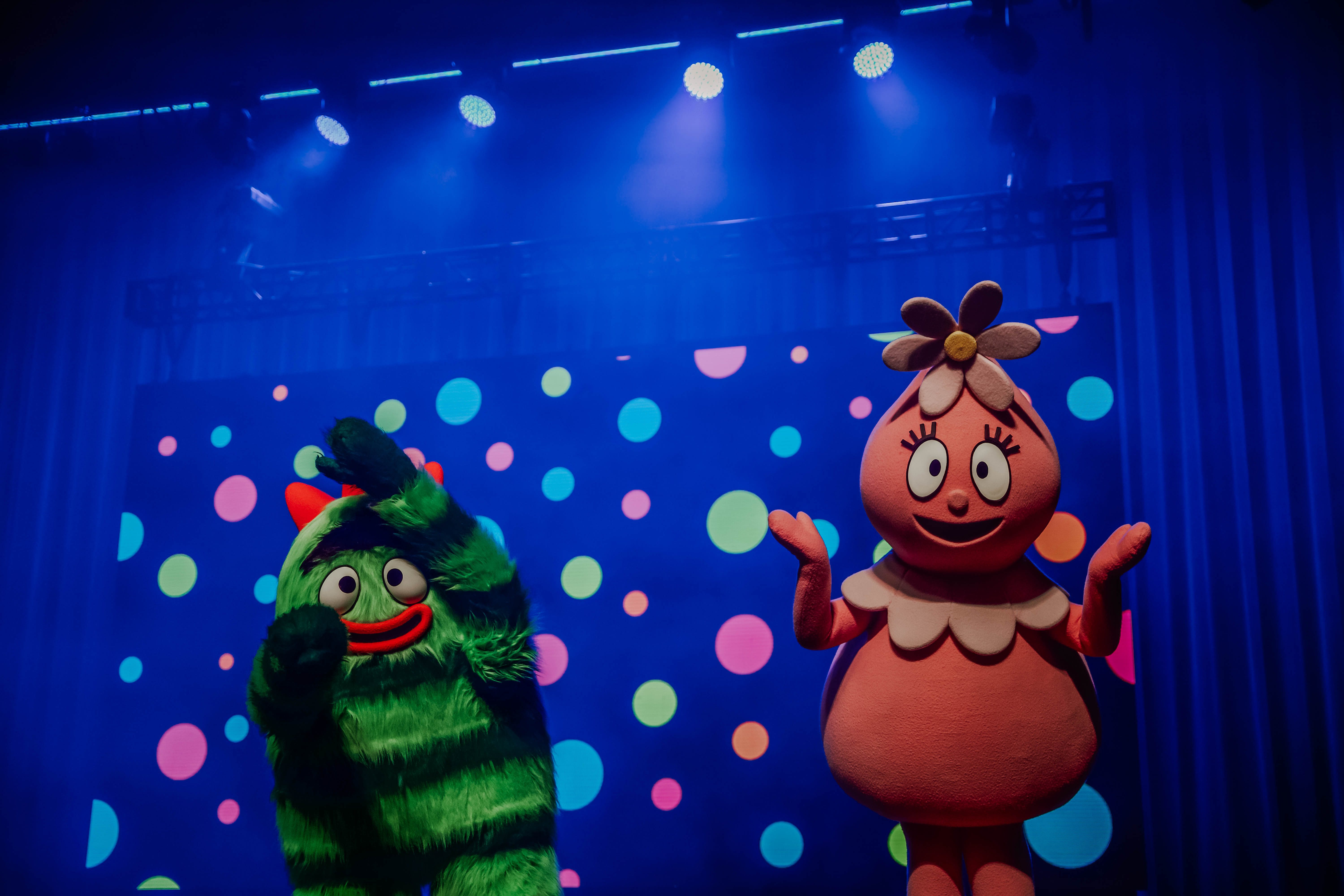Two colorful characters from _Yo Gabba Gabba!_ performing on stage with a vibrant background of polka dots and theatrical lighting.