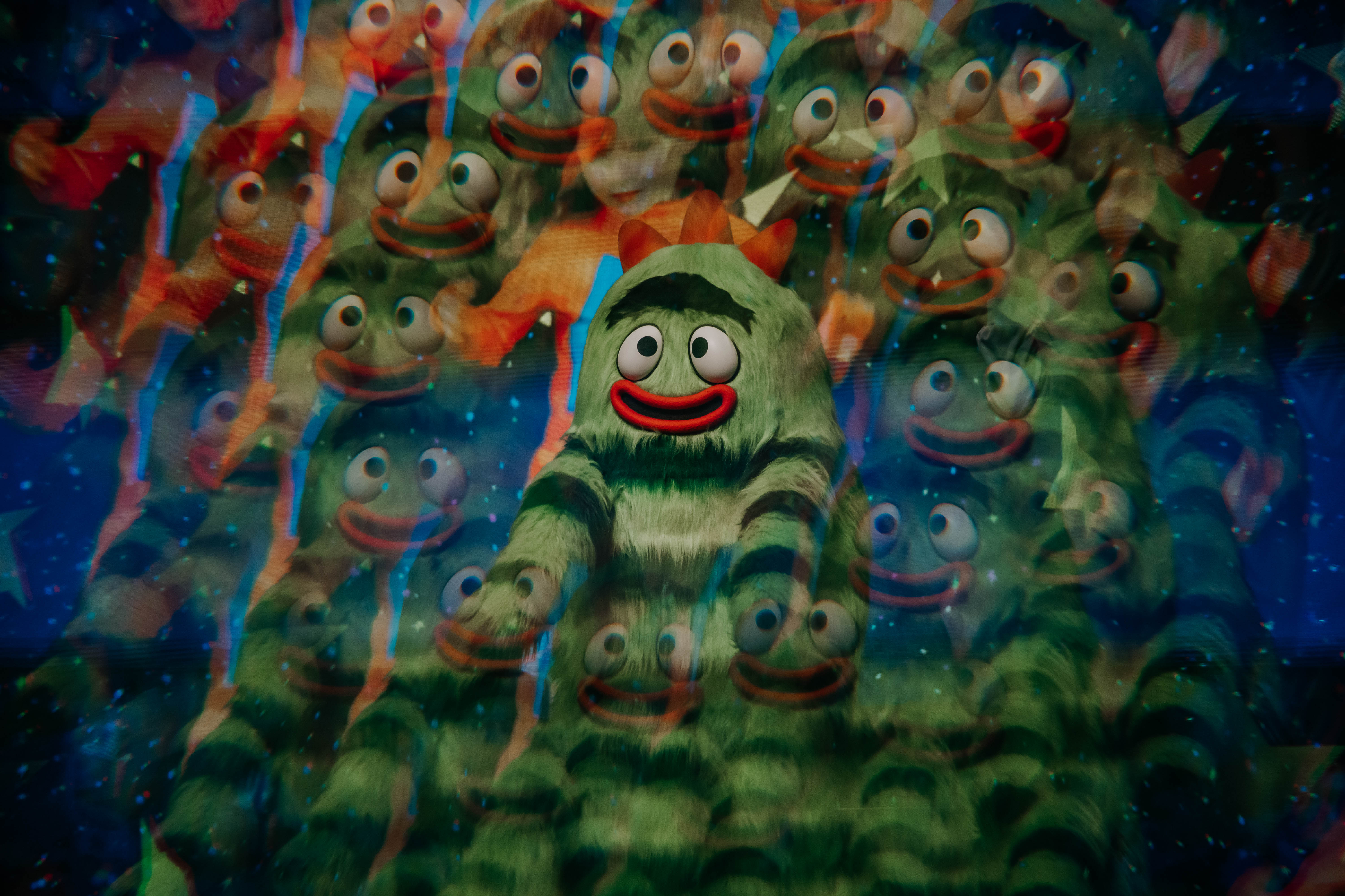 A vibrant scene featuring a whimsical green character surrounded by many similar characters, all with big eyes and cheerful expressions, creating a lively atmosphere.