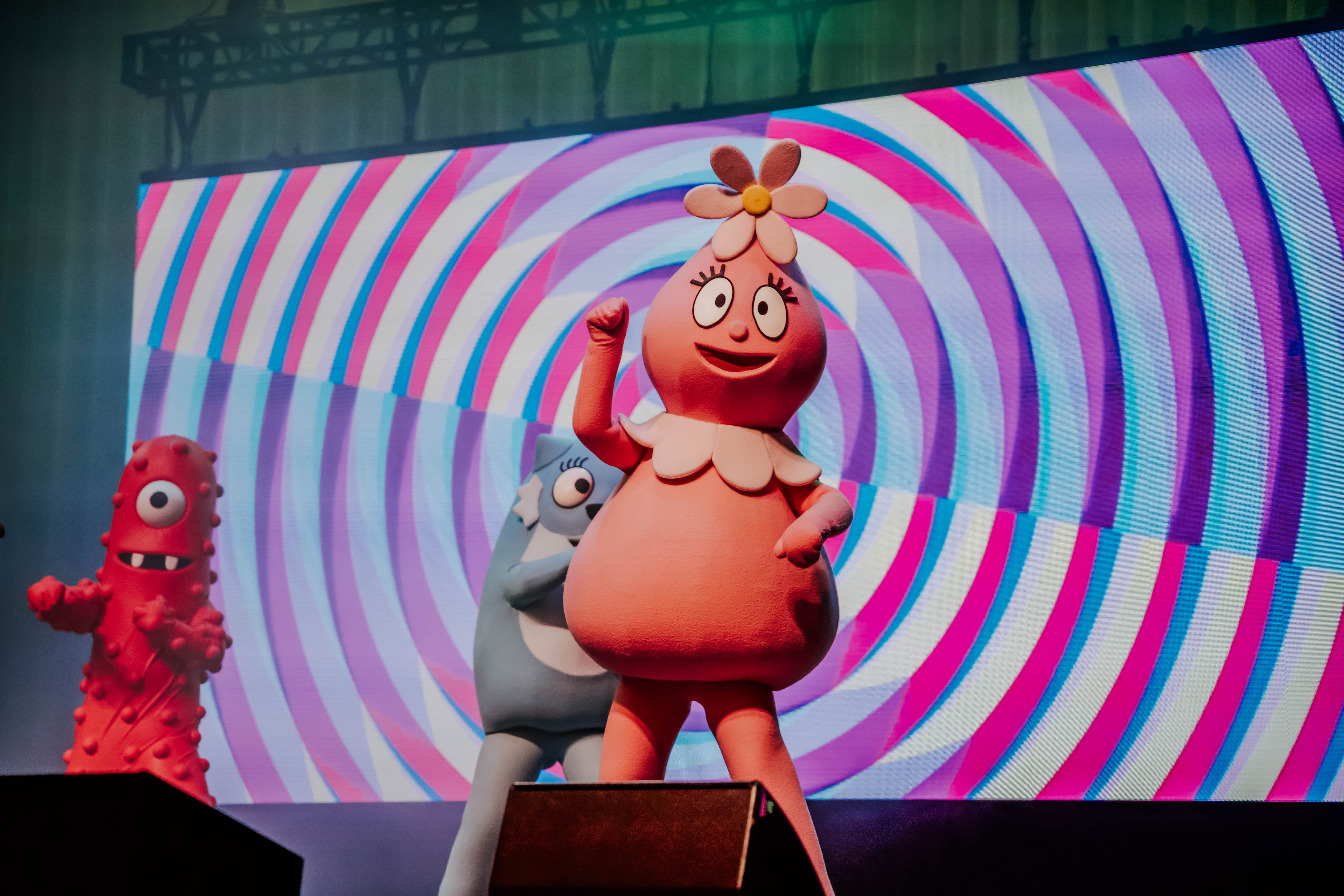 Colorful characters from _Yo Gabba Gabba!_ performing on stage with a vibrant background during a live concert.