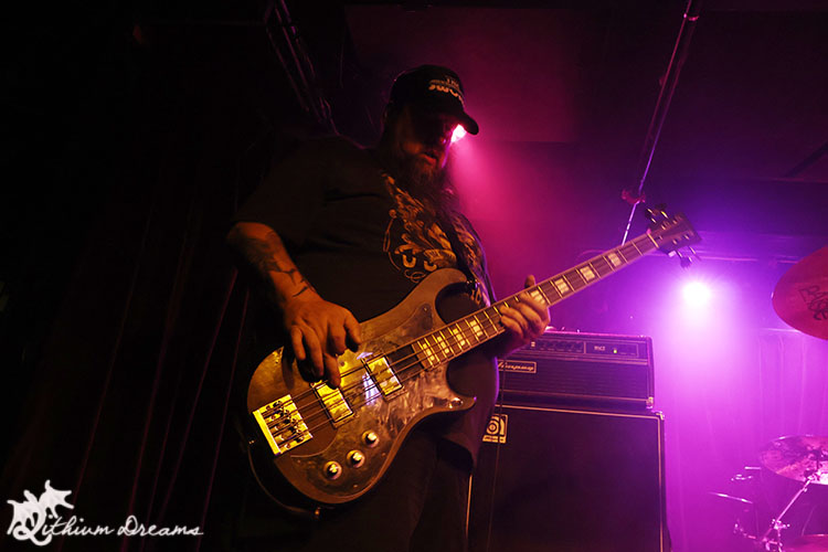 A bassist performing on stage under colorful lighting during a live music event.