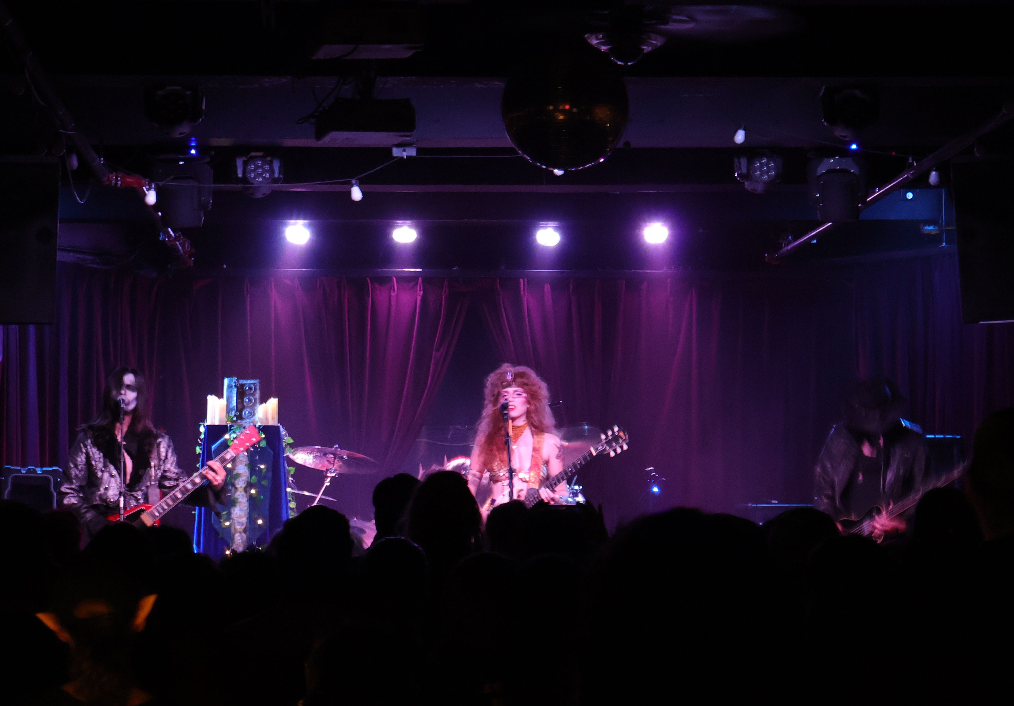 A band performing on stage with dramatic lighting and a crowd visible in the foreground.