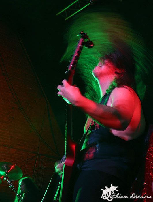 A guitarist with long hair performs energetically on stage, with vibrant lighting creating a dynamic atmosphere.