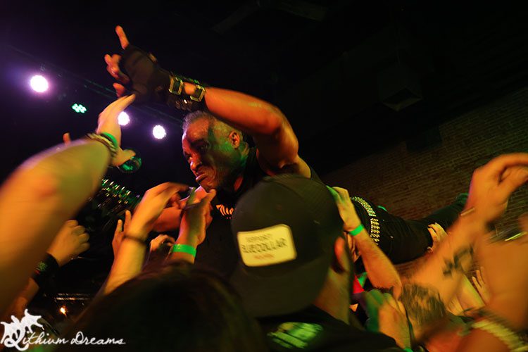 Crowd-surfing metal vocalist engaging with fans during a live concert performance, vibrant stage lighting in background.